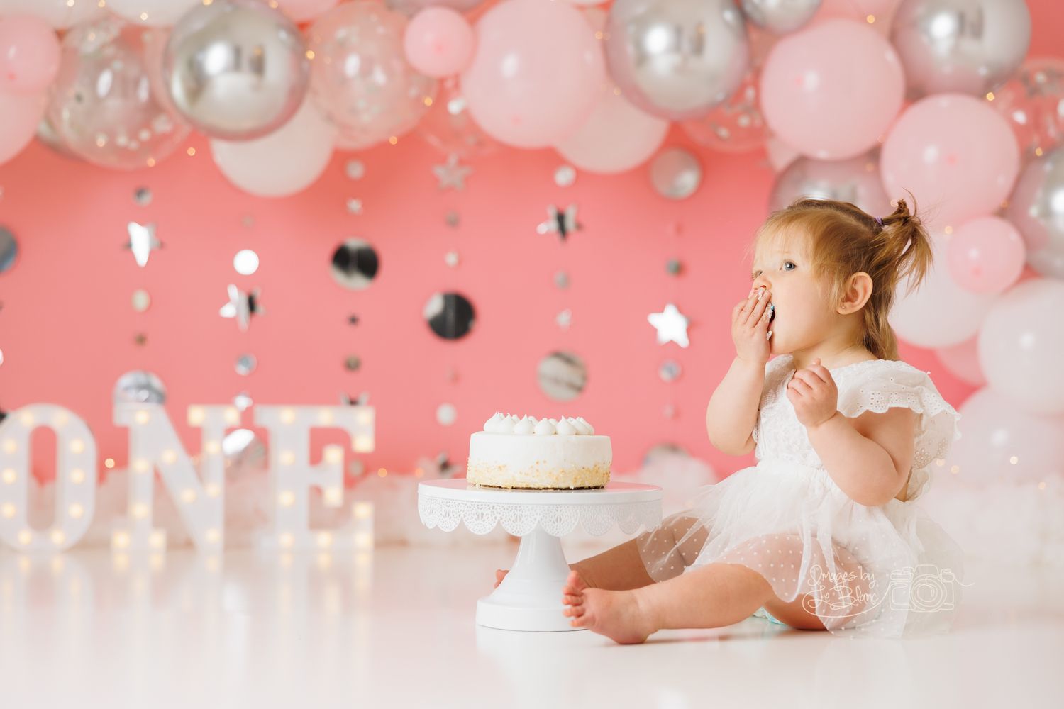 Pink and white themed first birthday cake smash photo session setup with pearls and balloons.
