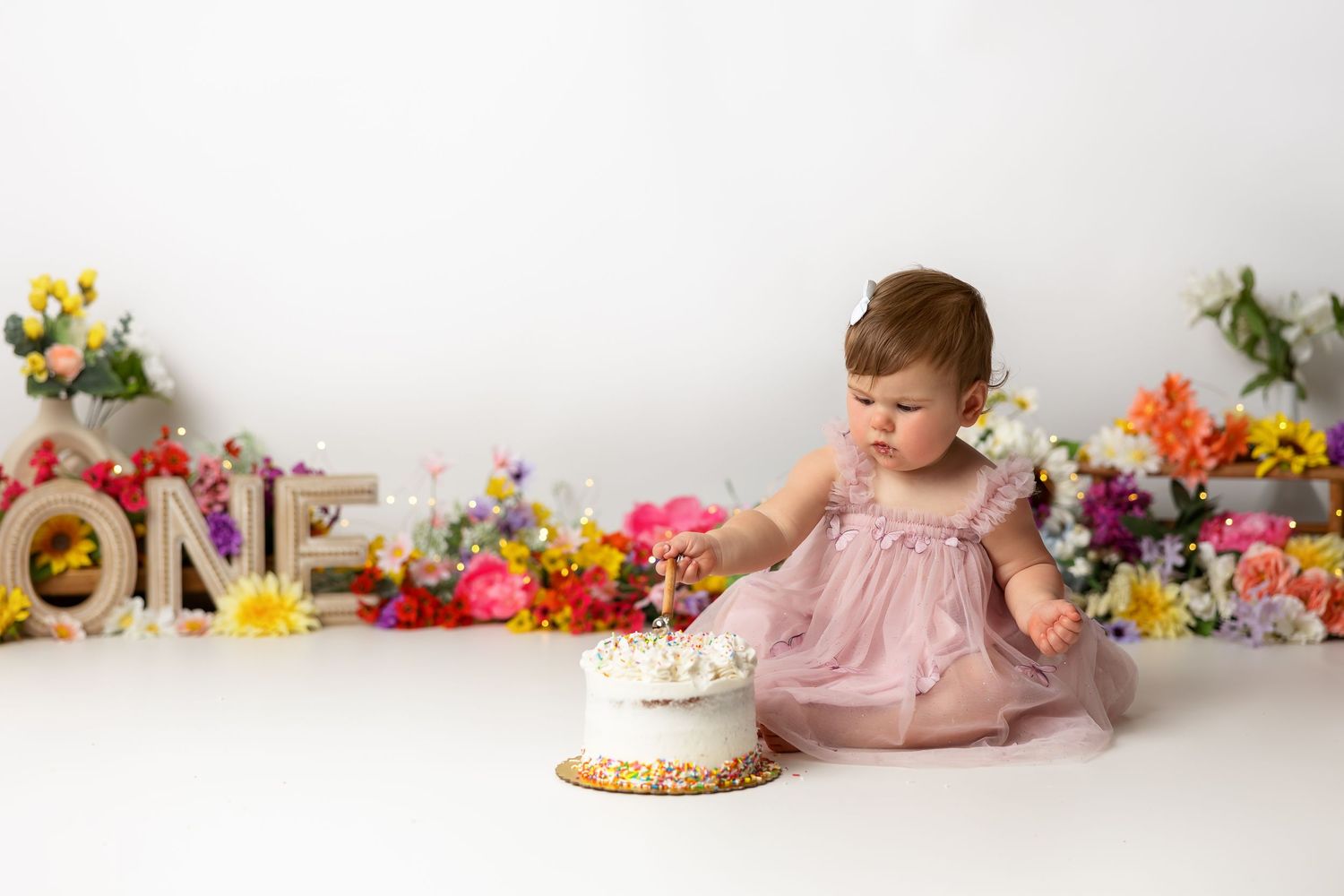Floral garden party setup with pink decor and white birthday cake against neutral backdrop.