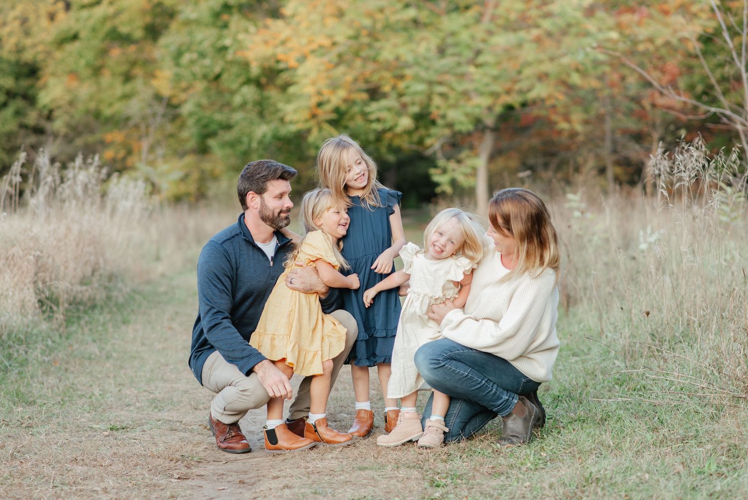 A small group interacts playfully in a natural outdoor setting with fall colors in the background.