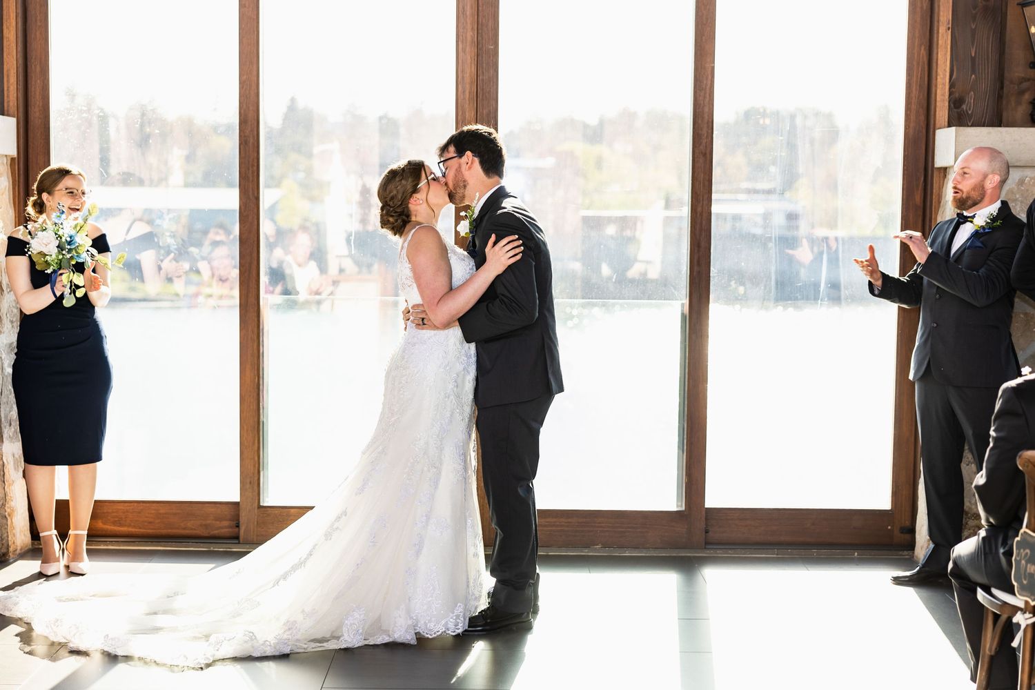 Newlyweds share their first dance in a sunlit room with floor-to-ceiling windows.