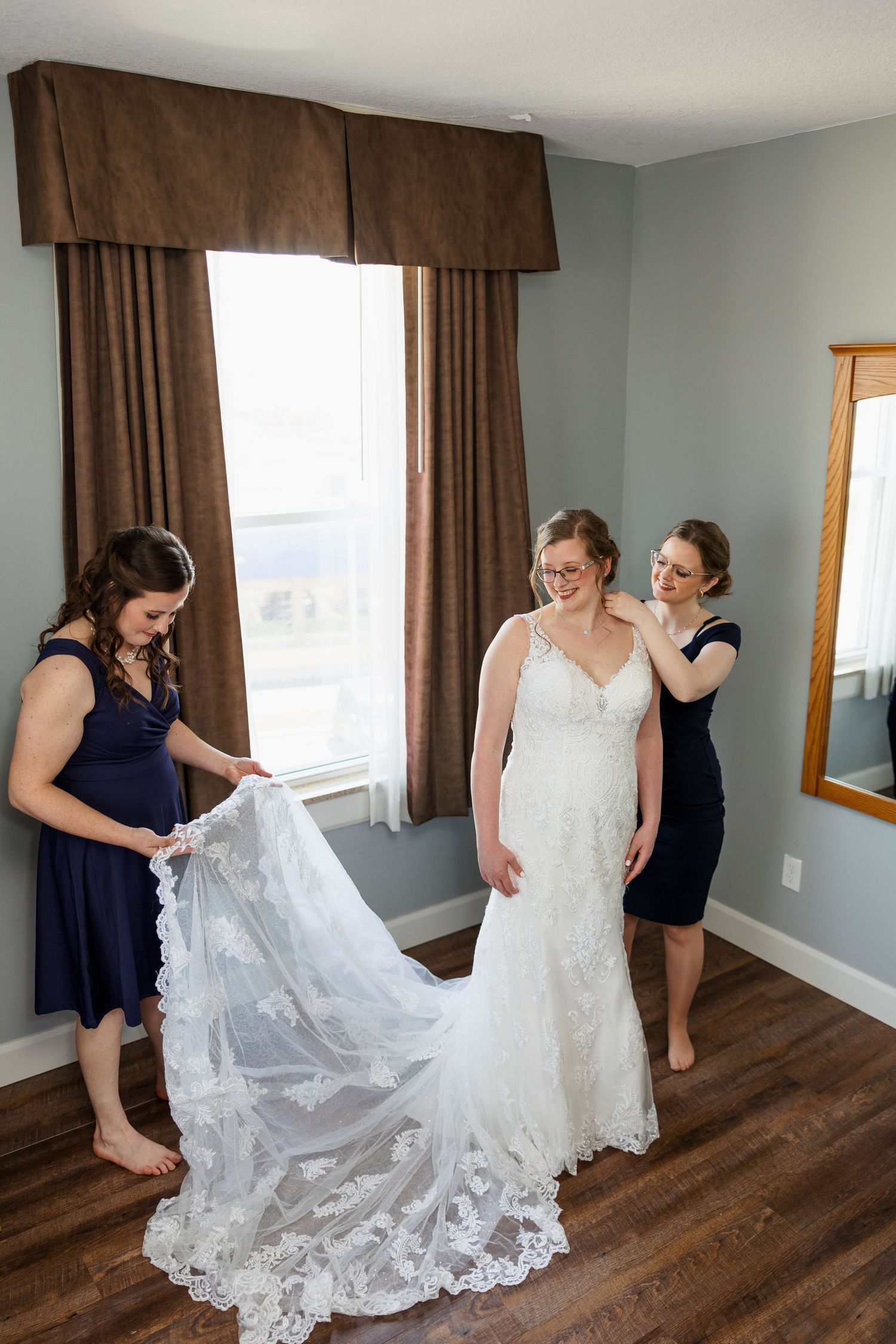 Three women in a hotel room helping with a wedding dress with lace details.