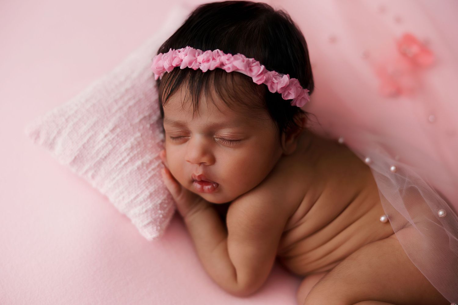 Sleeping newborn on pink pillow with floral headband and delicate veil.