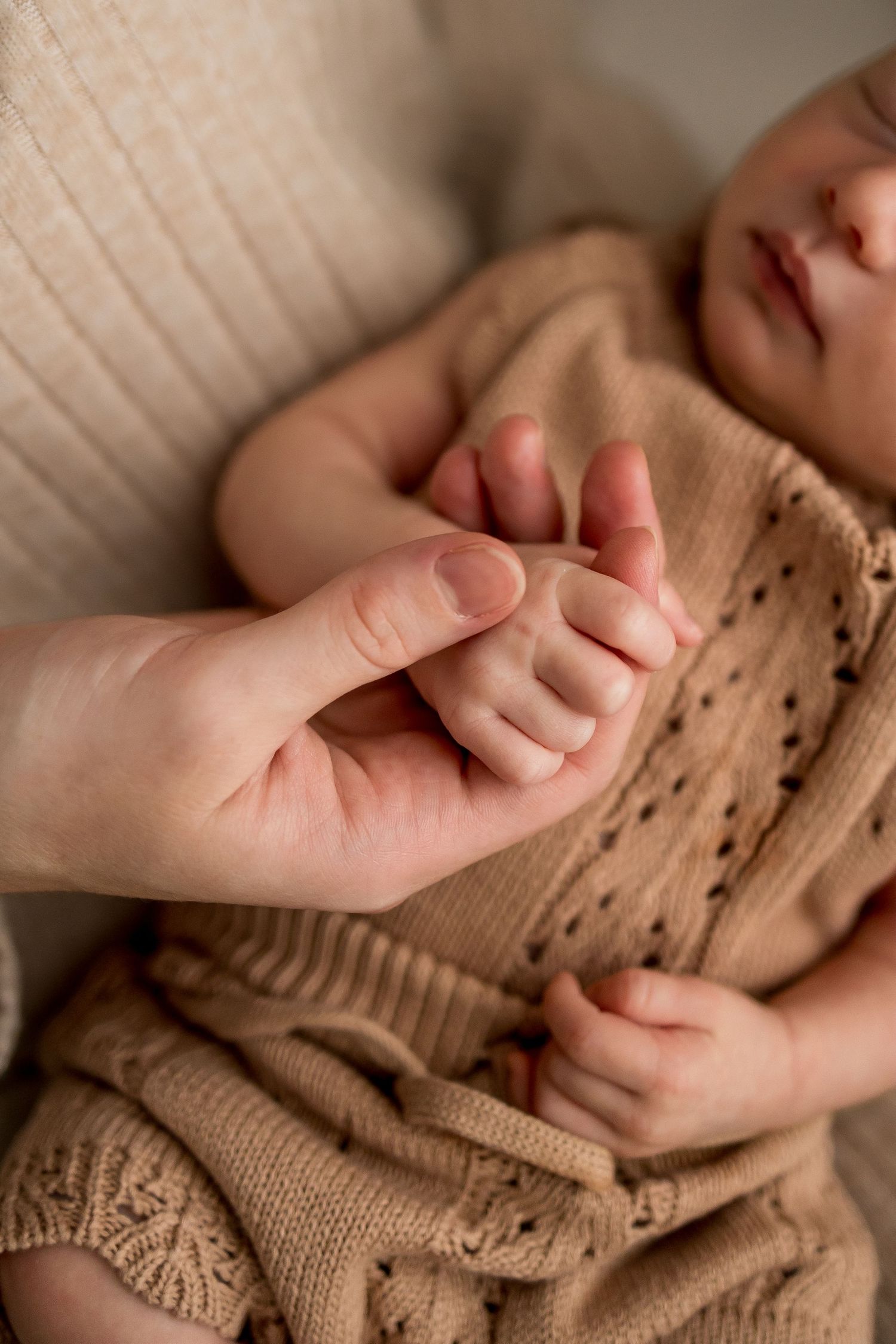Close-up photos of tiny hands grasping a knitted beige sweater in warm, natural lighting.