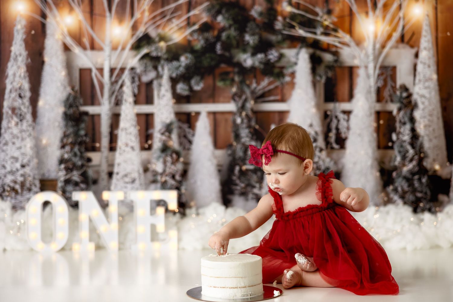 Winter wonderland themed first birthday setup with snowy trees and twinkling lights.