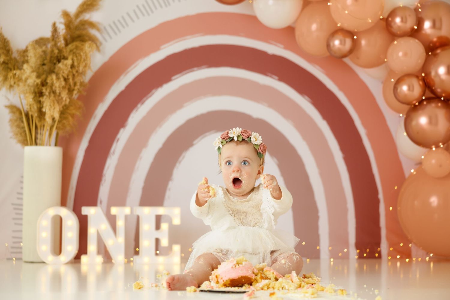 Excited baby during cake smash photo session with retro rainbow backdrop and balloon decor.
