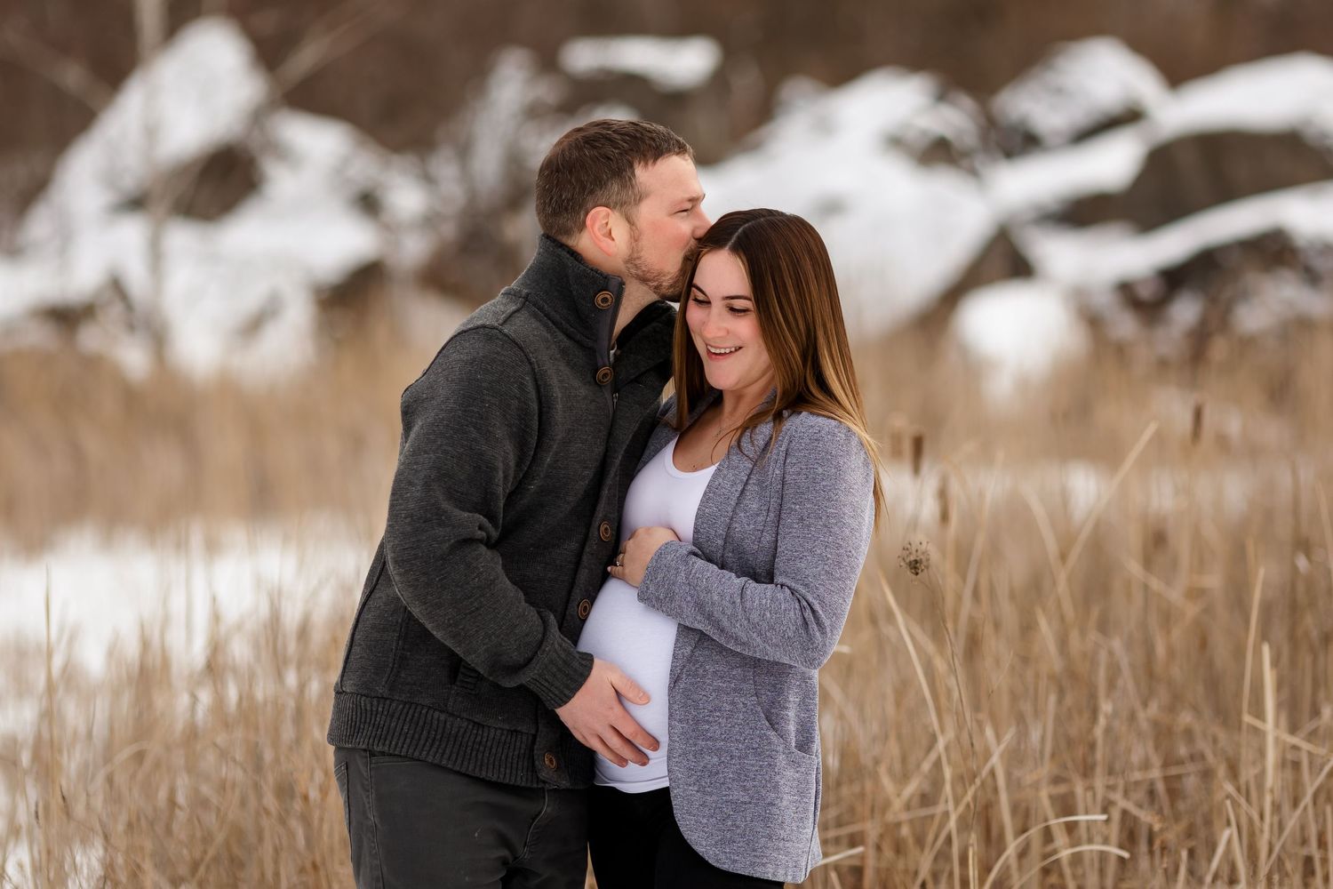Intimate maternity moment captured in winter setting with natural brown backdrop.