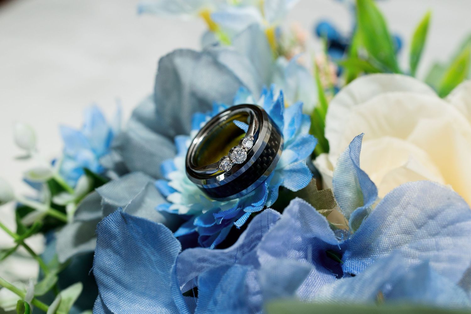 Wedding rings nestled in blue flowers create an artistic macro composition.