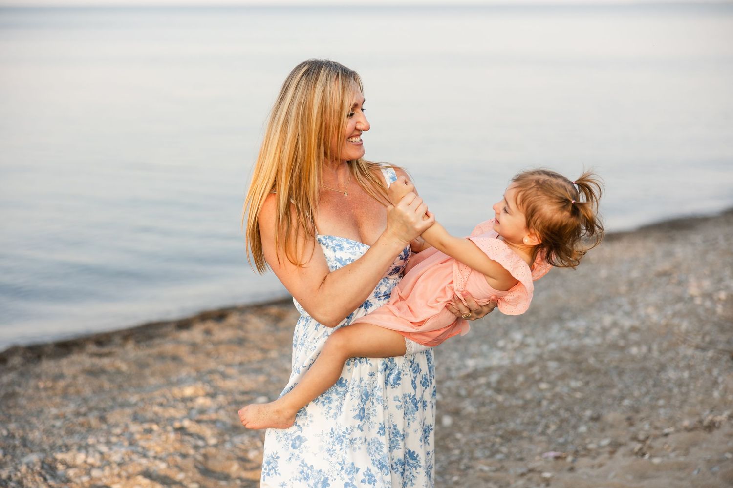 Adult and child share a joyful moment together on a beach at sunset by the water.