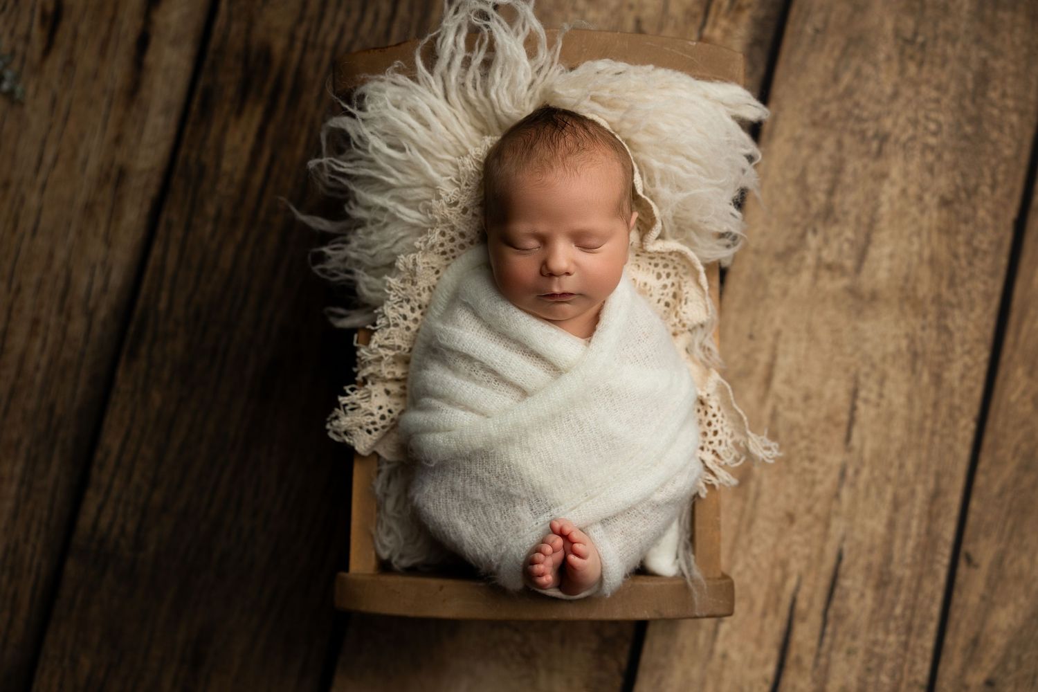 Peaceful newborn sleeping in wooden crate with white wrap and furry backdrop.