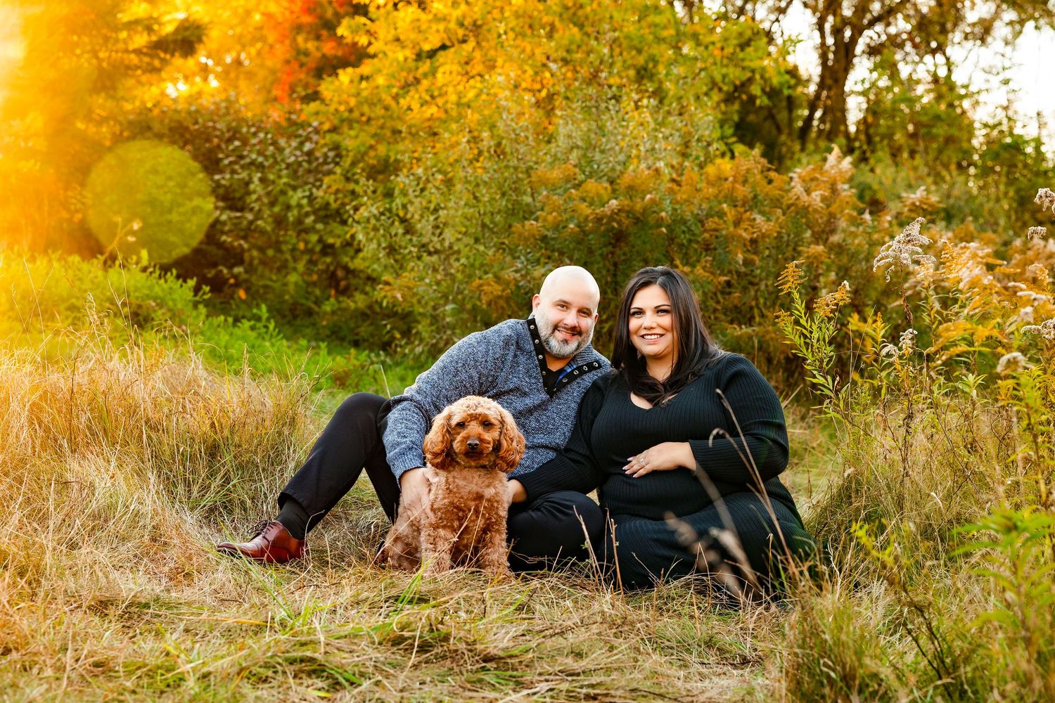 Outdoor maternity photography session with couple and dog in autumn field.