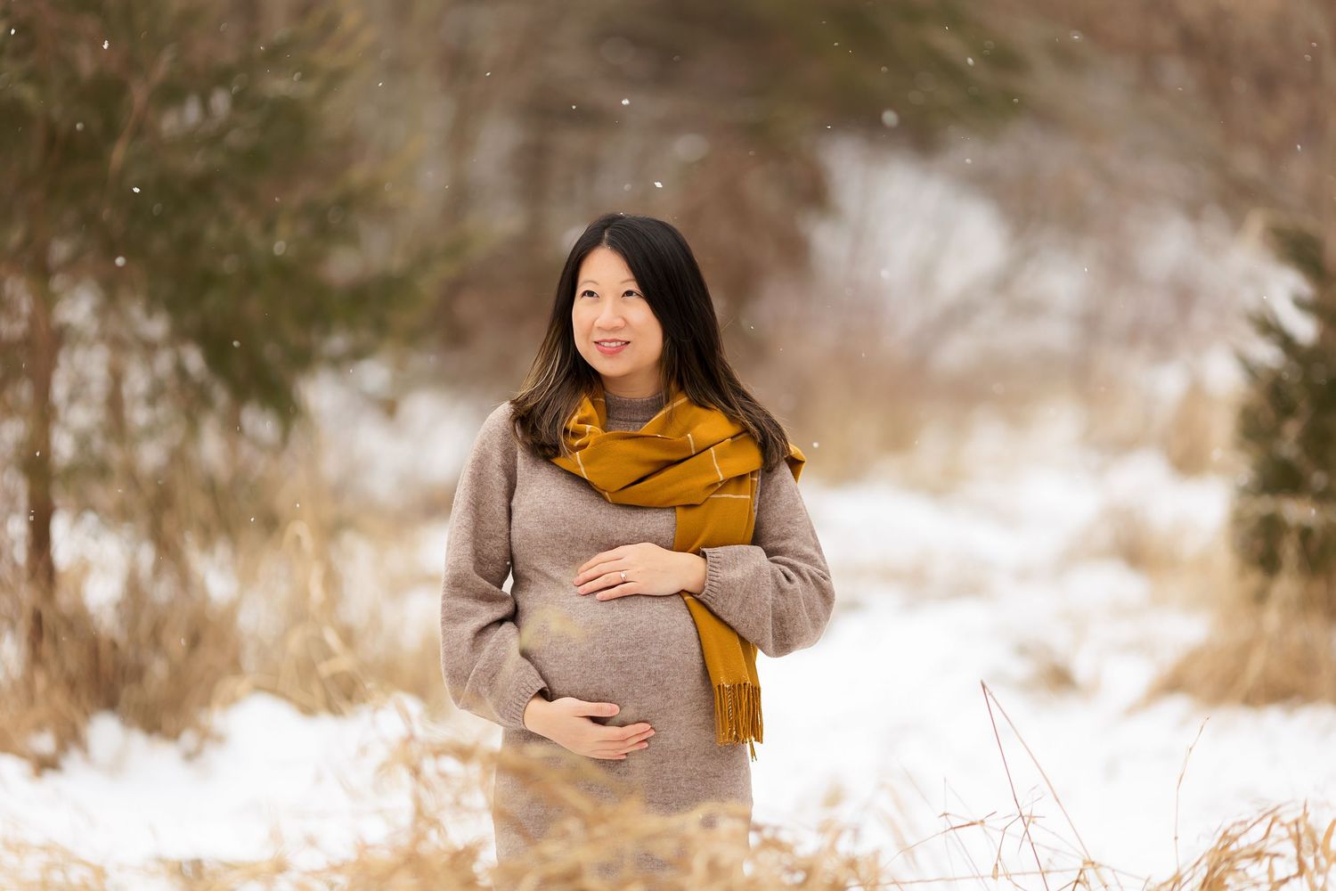 A winter maternity session featuring warm accessories against a snowy landscape.