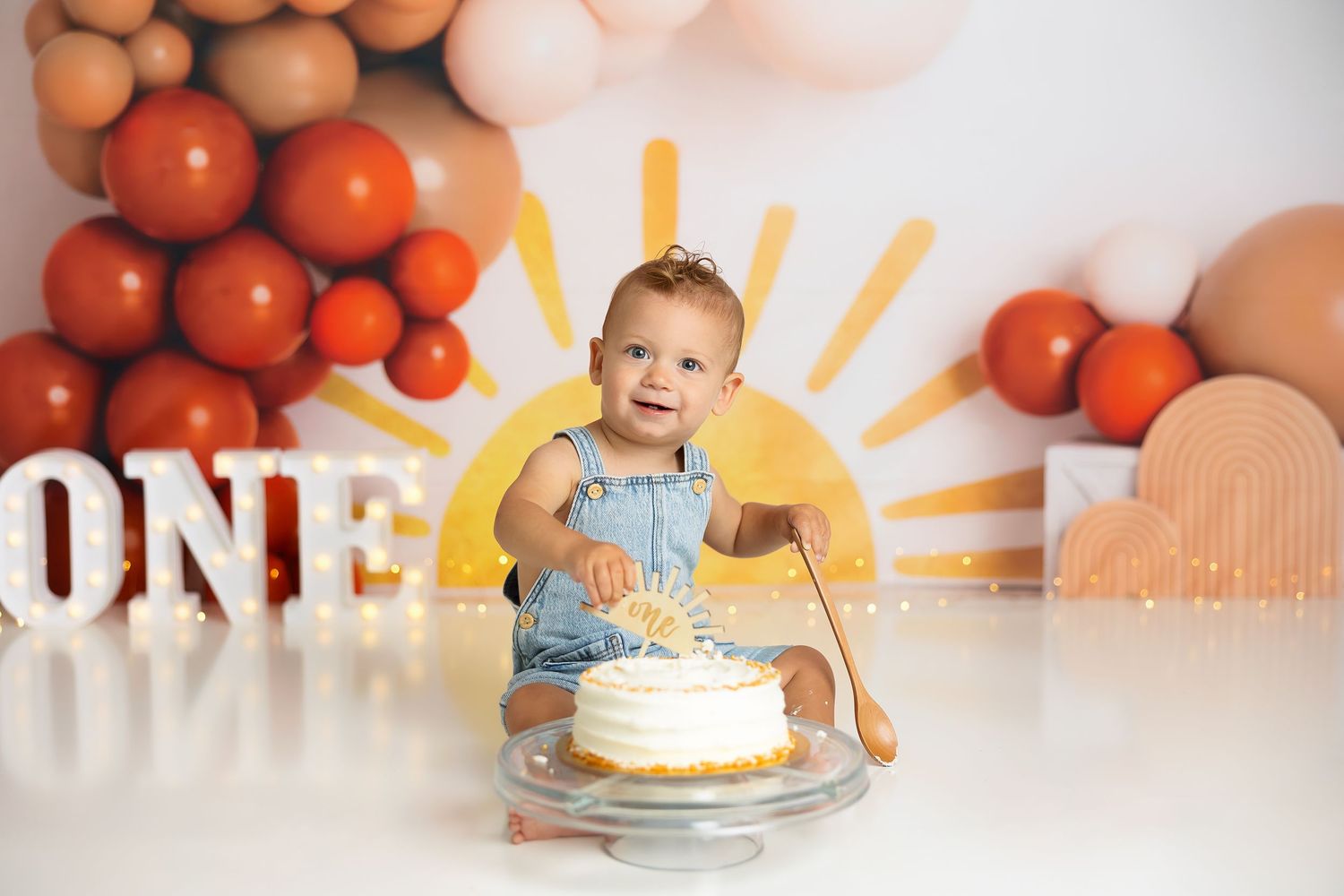 Orange balloon arch with rustic farmhouse decor and cake setup for first birthday celebration.