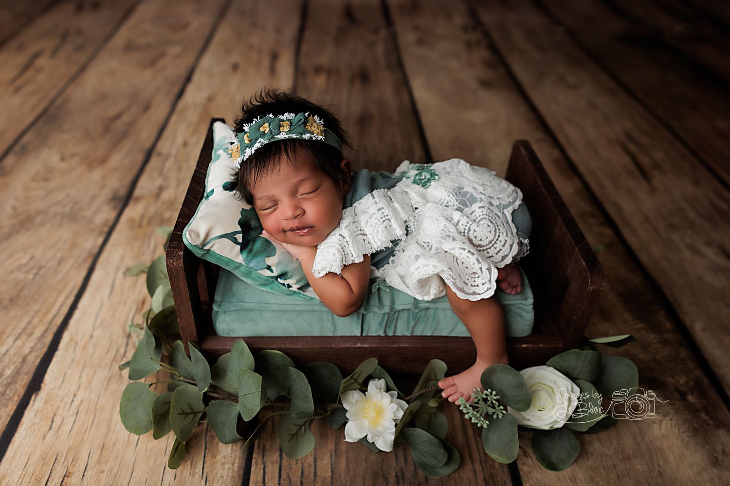 Newborn sleeping in wooden drawer with floral decorations and lace wrap.