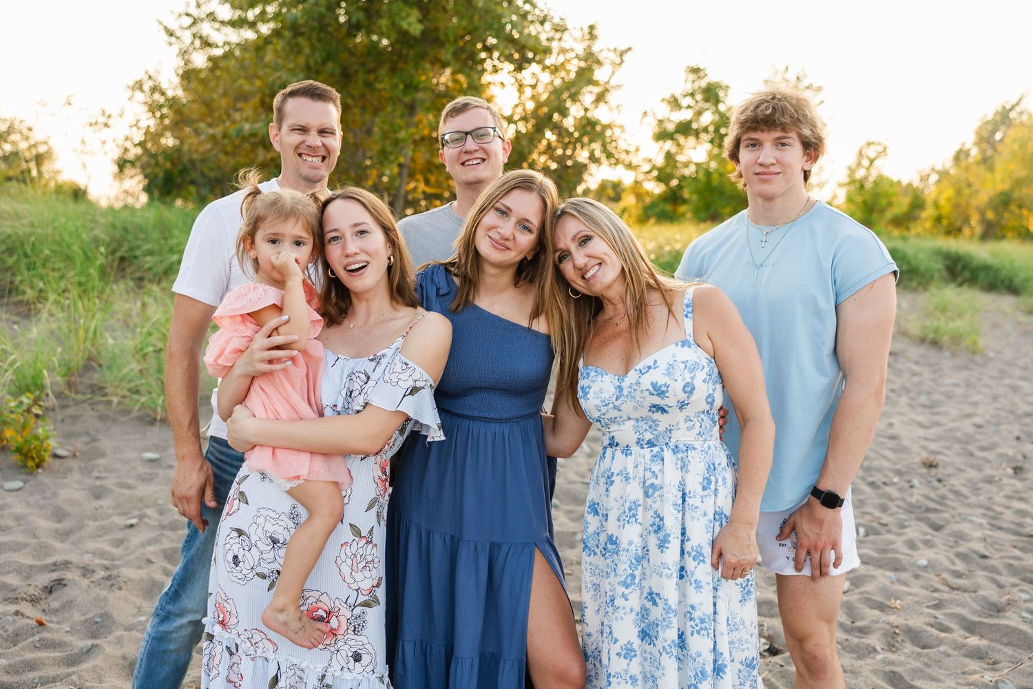 A group poses together on a sandy beach path at sunset wearing coordinating blue and white summer outfits.