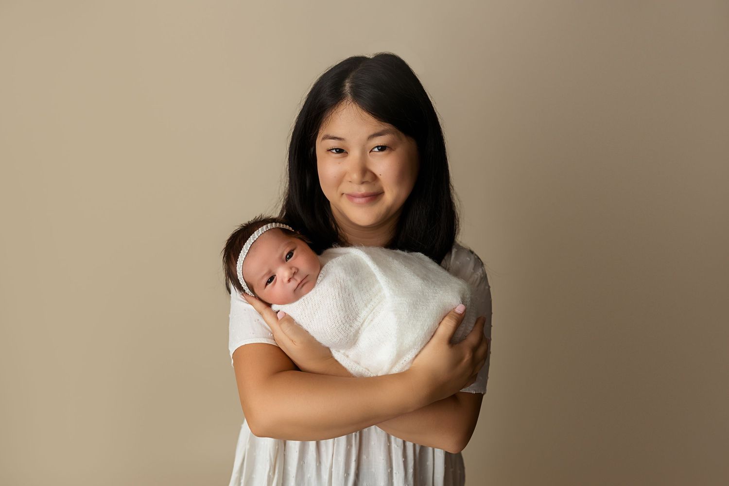 A tender newborn portrait against a neutral beige backdrop.