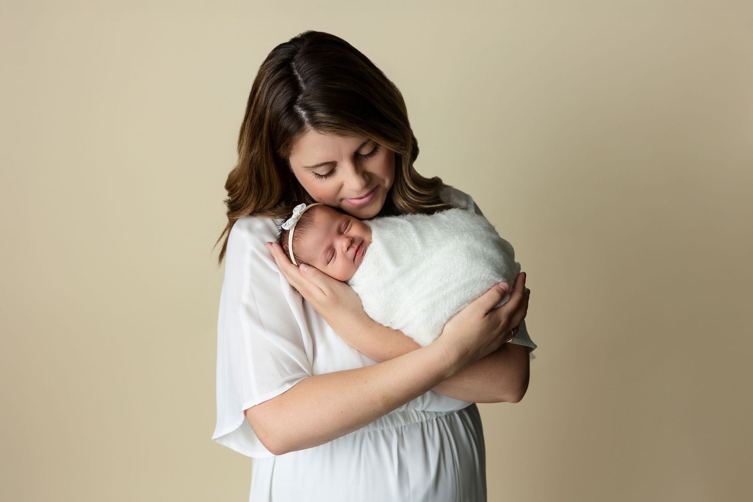 Tender moment in studio with white-dressed figures against beige background.
