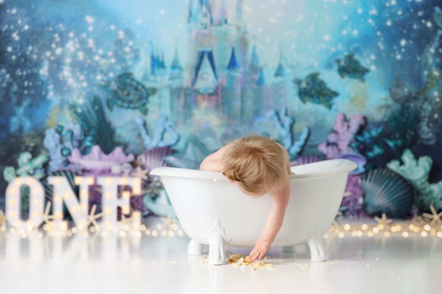 Baby playing in vintage white bathtub against dreamy underwater castle backdrop.
