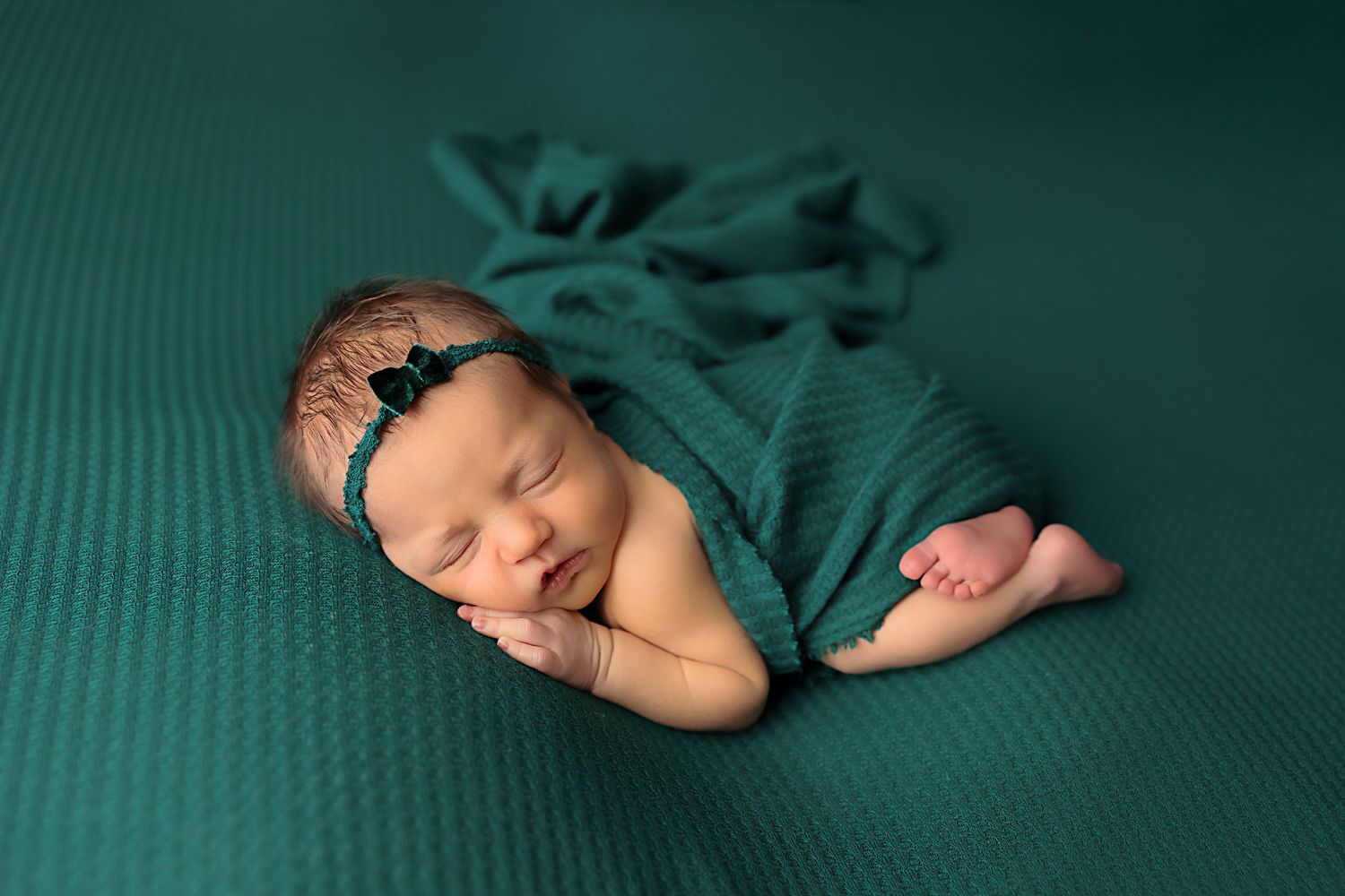 Peaceful newborn portrait with teal wrap and headband on green background.