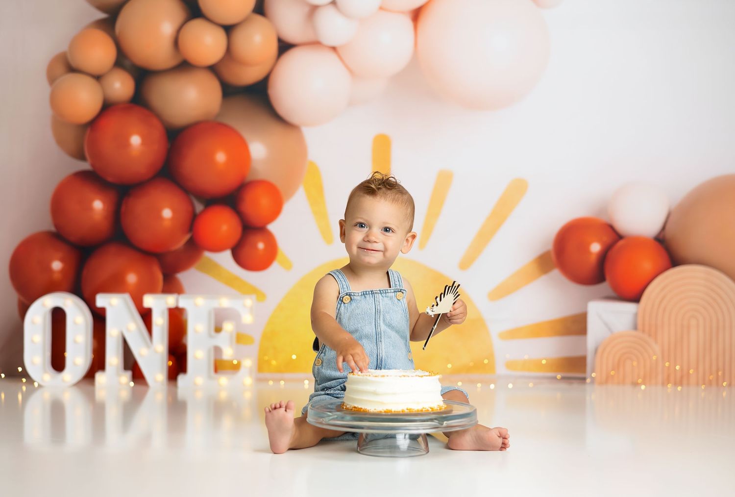 A cake smash photo setup with balloons and sun backdrop featuring a first birthday celebration.