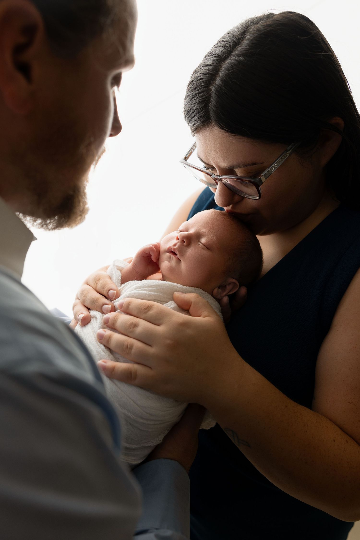 An intimate family portrait showing tender moments with their sleeping newborn baby.