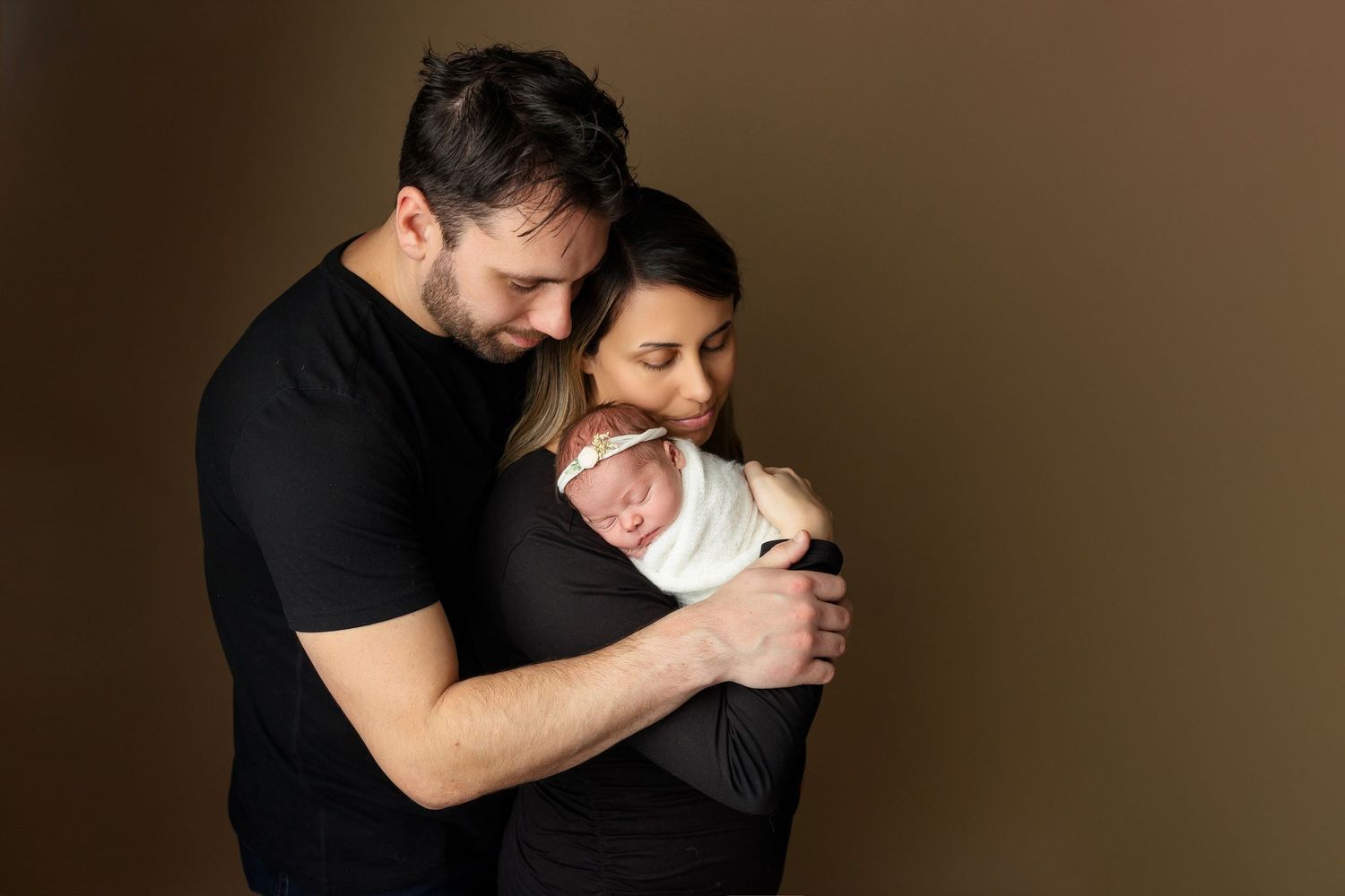Intimate family moment with newborn against dark studio background.