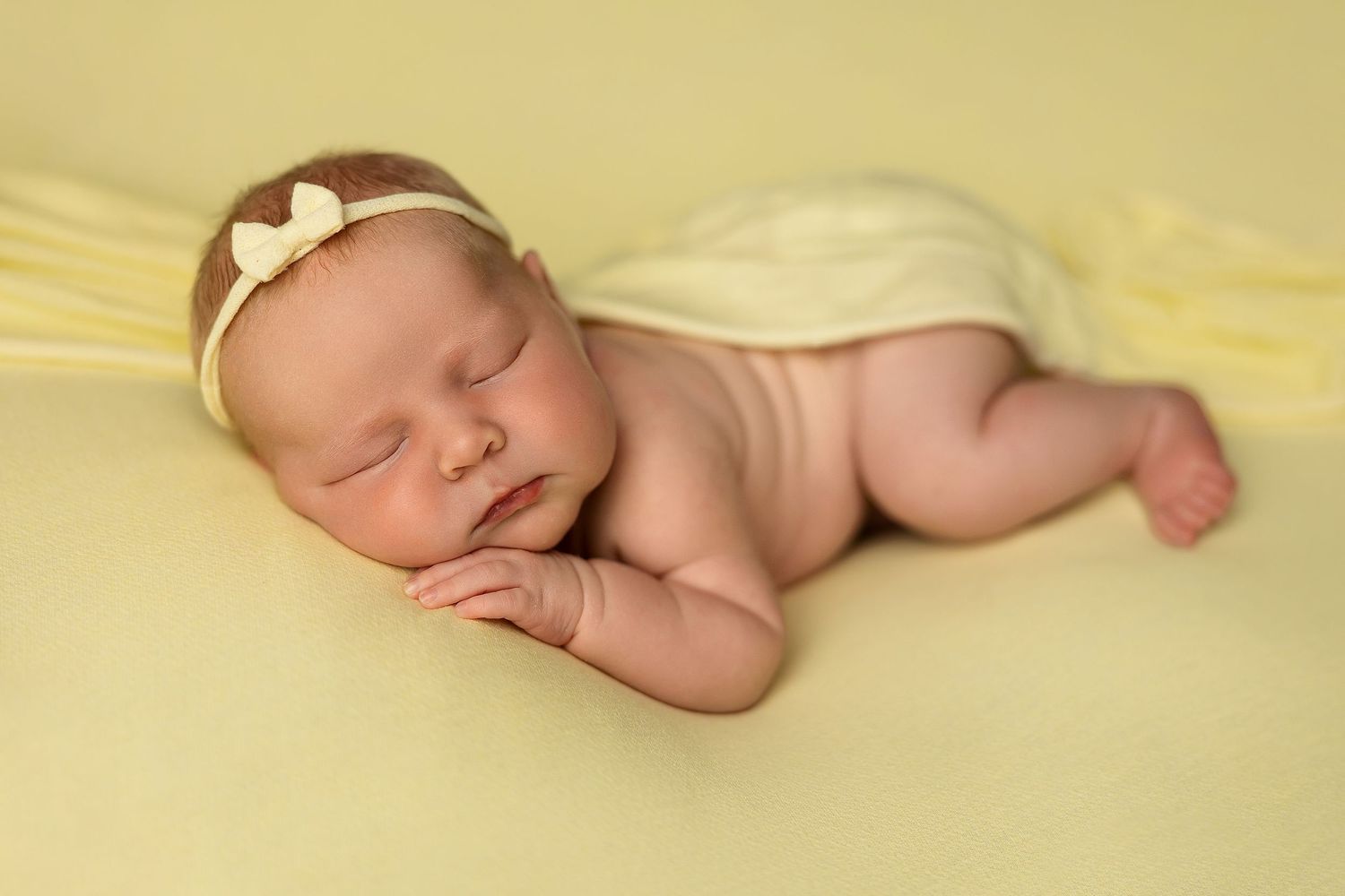 Peaceful sleeping newborn on soft yellow blanket wearing delicate headband.