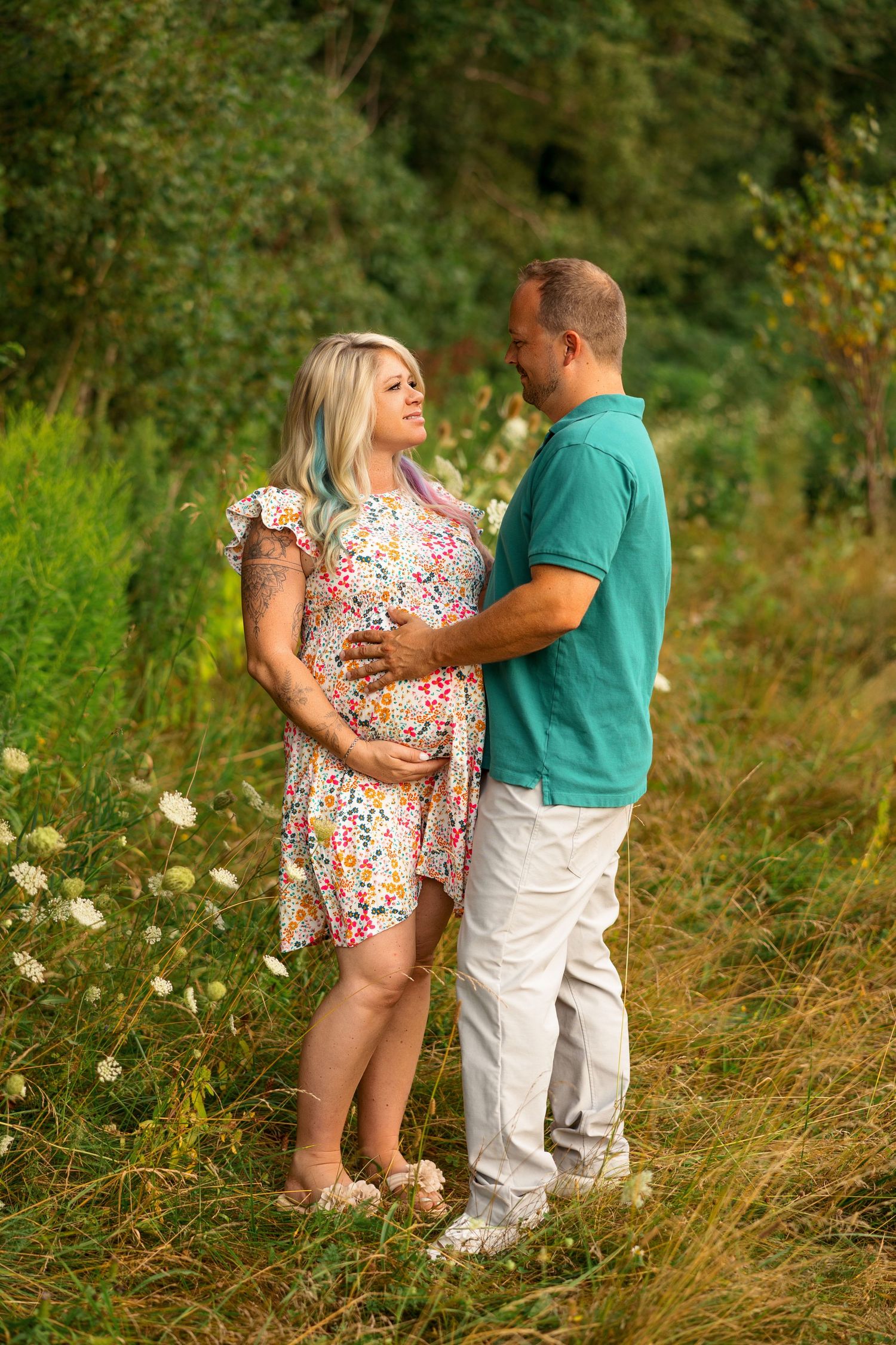 A couple shares tender moments together in a sunny meadow filled with tall grass and wildflowers.