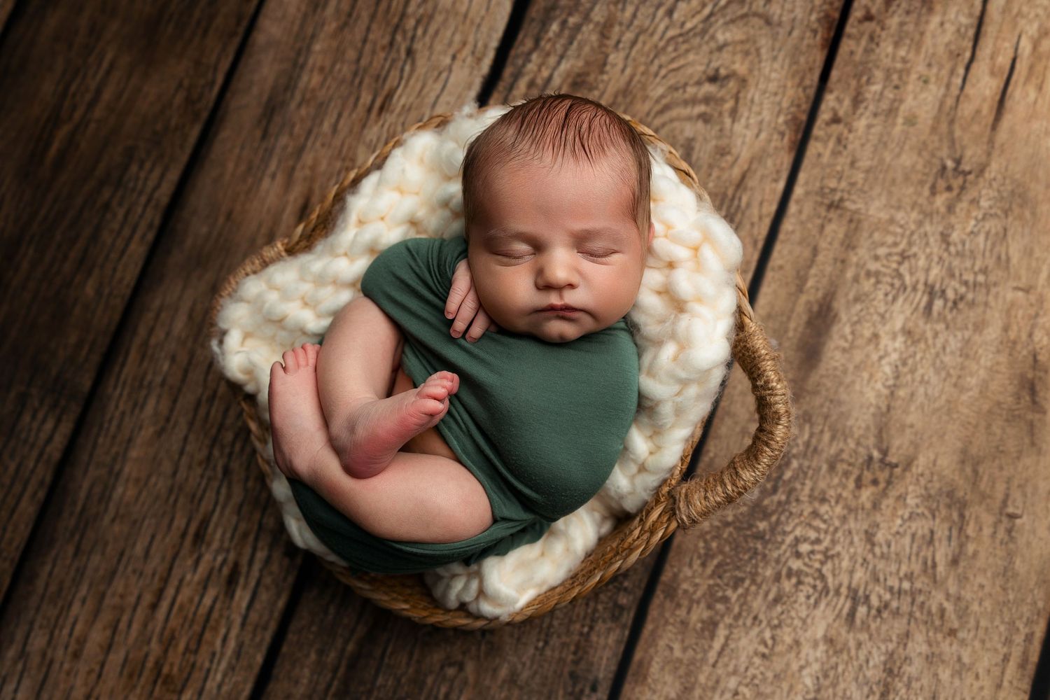 Sleeping newborn nestled in cozy basket with white padding on wooden surface.