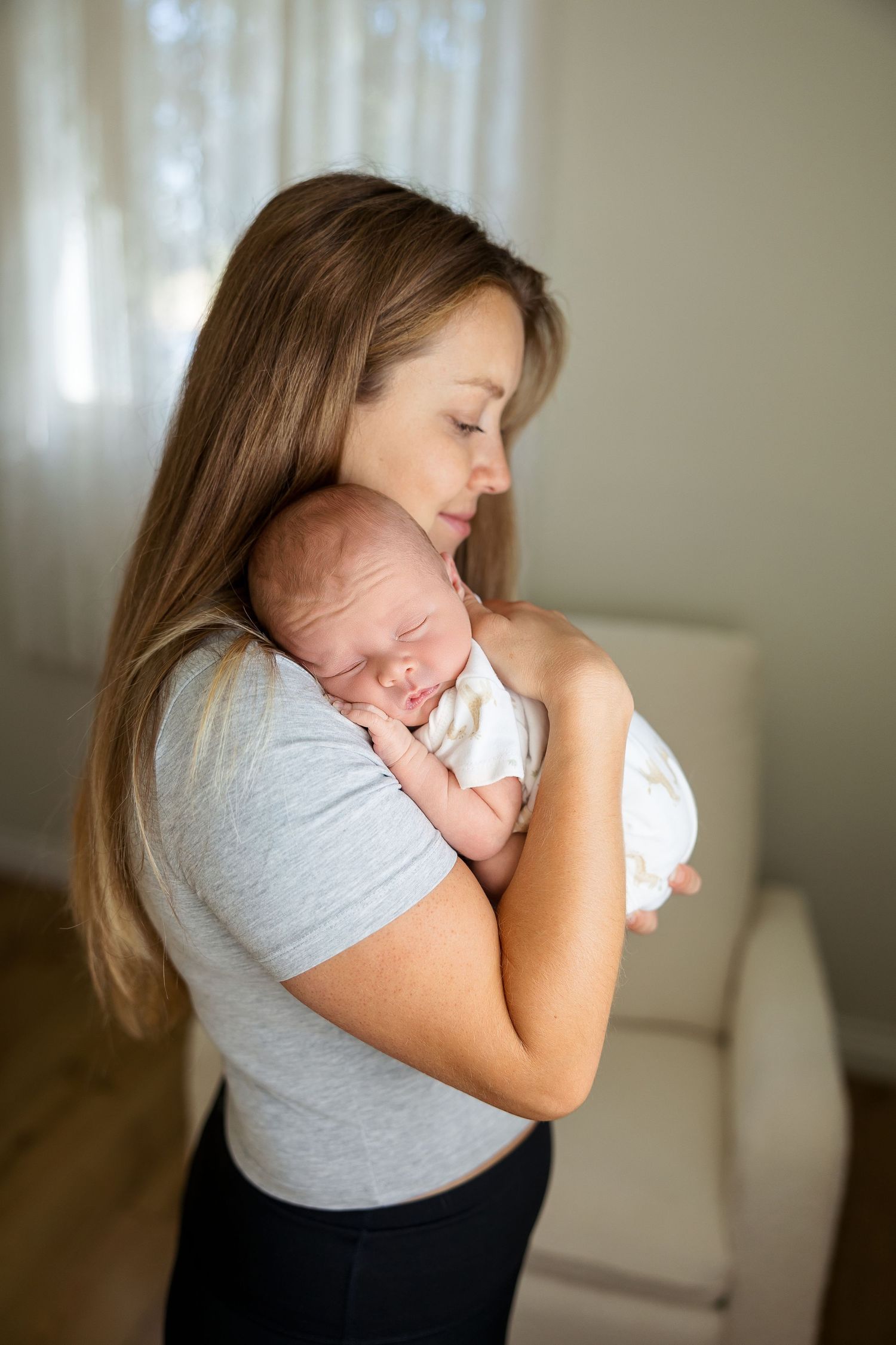 A mother in a gray t-shirt holds and cuddles her newborn baby in a tender moment at home.