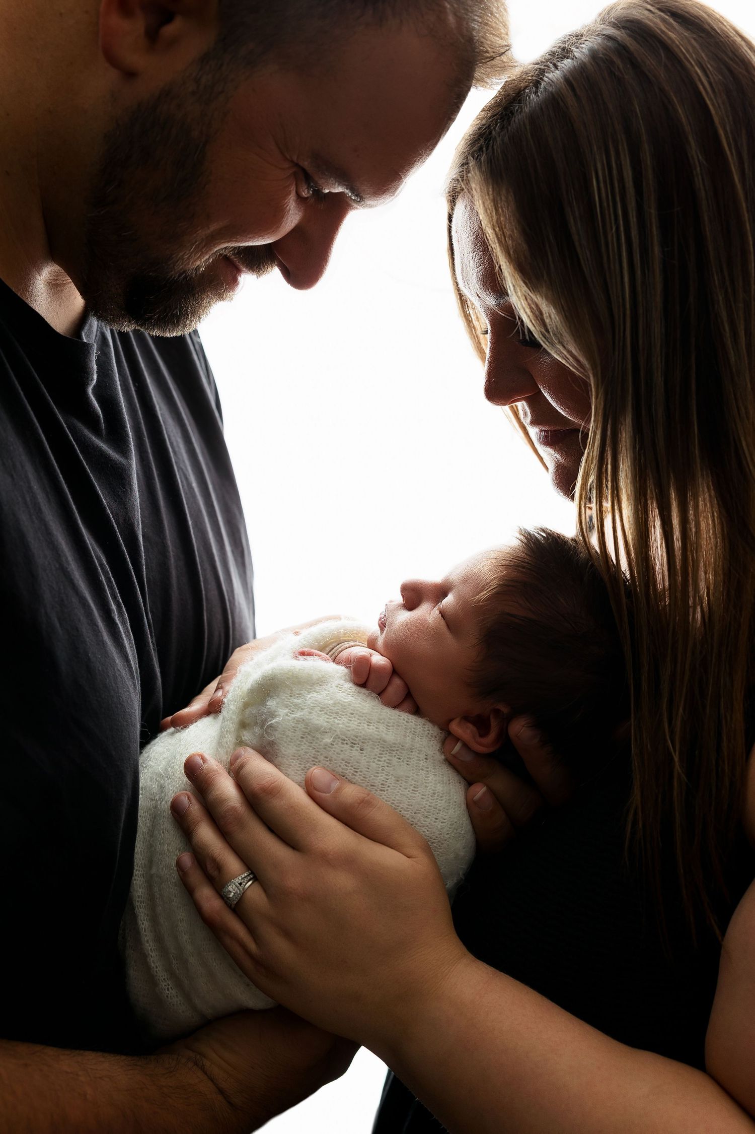 Silhouetted parents tenderly holding their sleeping newborn baby in a soft backlit family moment.