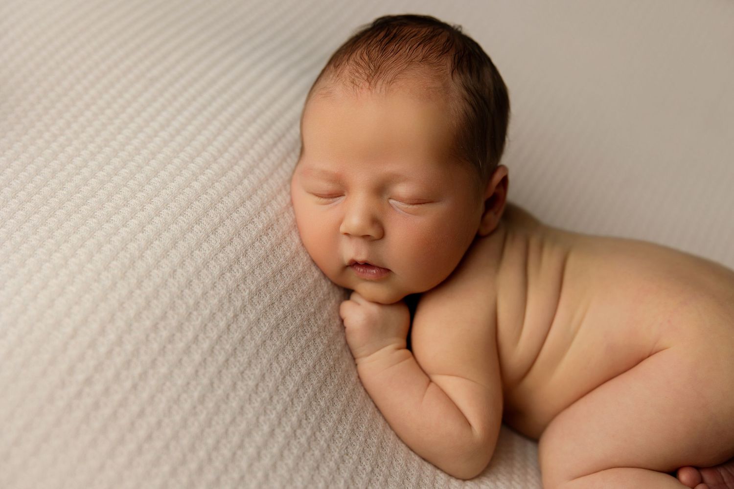Peaceful sleeping newborn lying on textured cream surface in natural light.