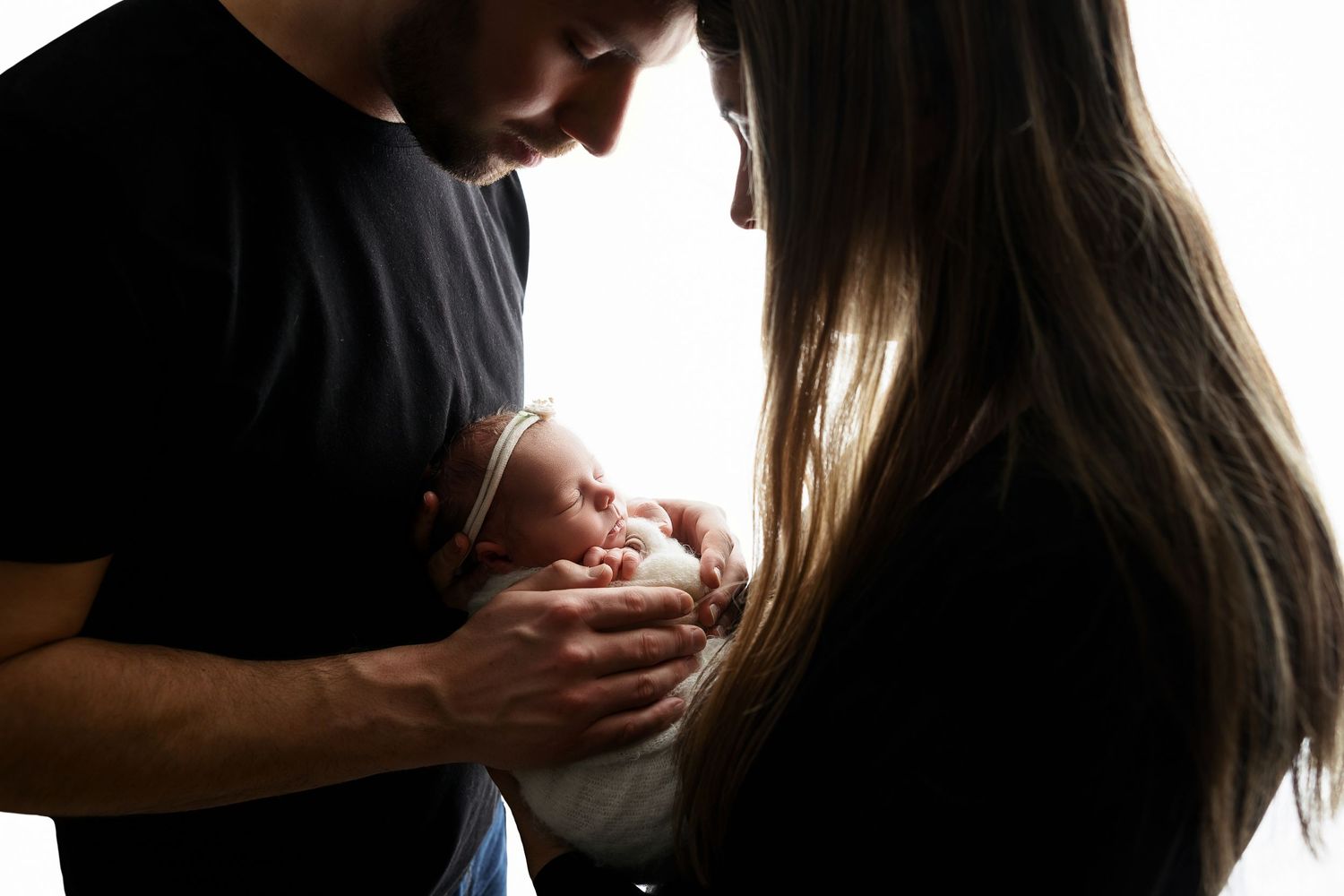 Backlit silhouette of parents tenderly holding their newborn baby.