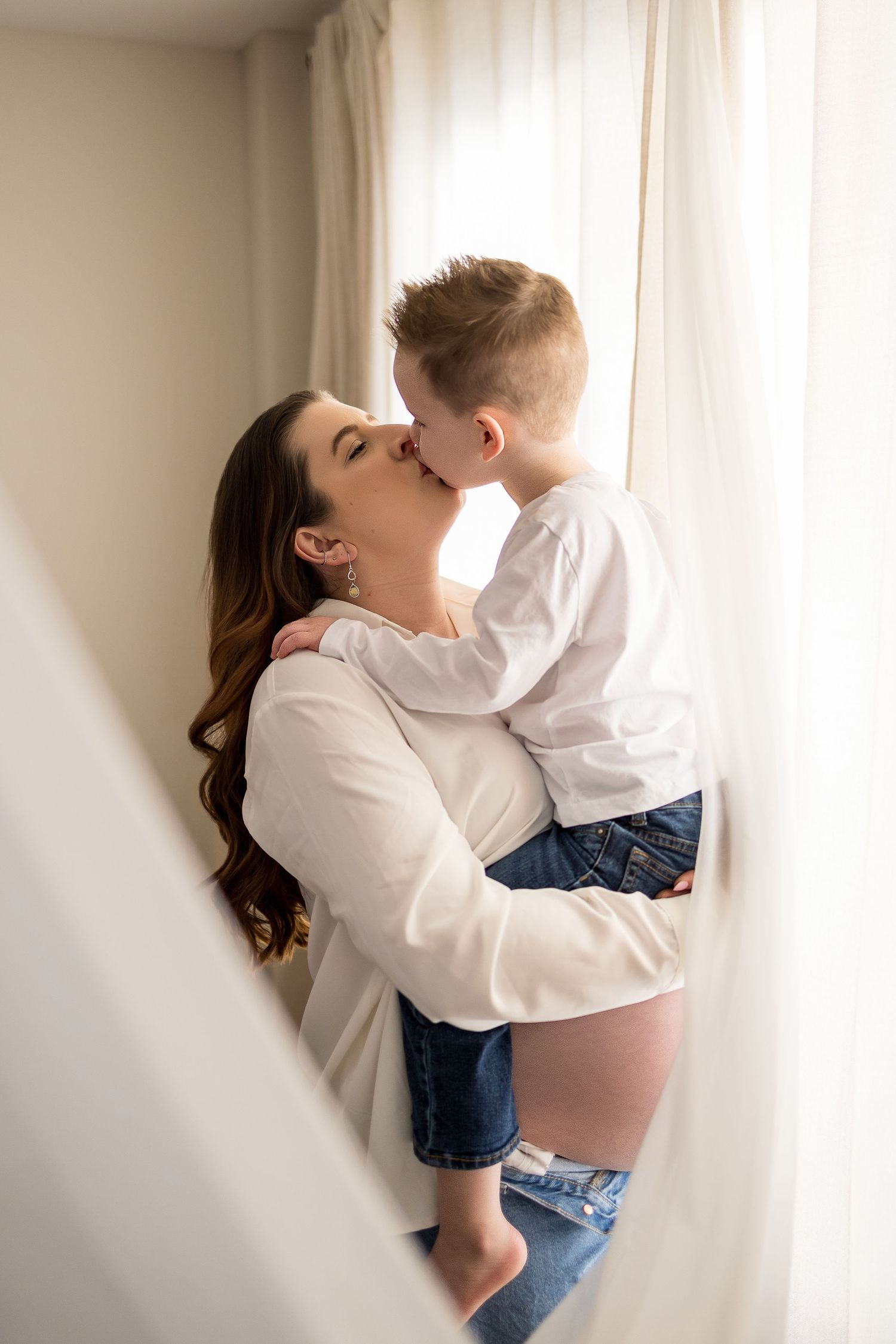 A tender moment captured in a series of soft, minimalist photos showing affection and connection against a white wall.