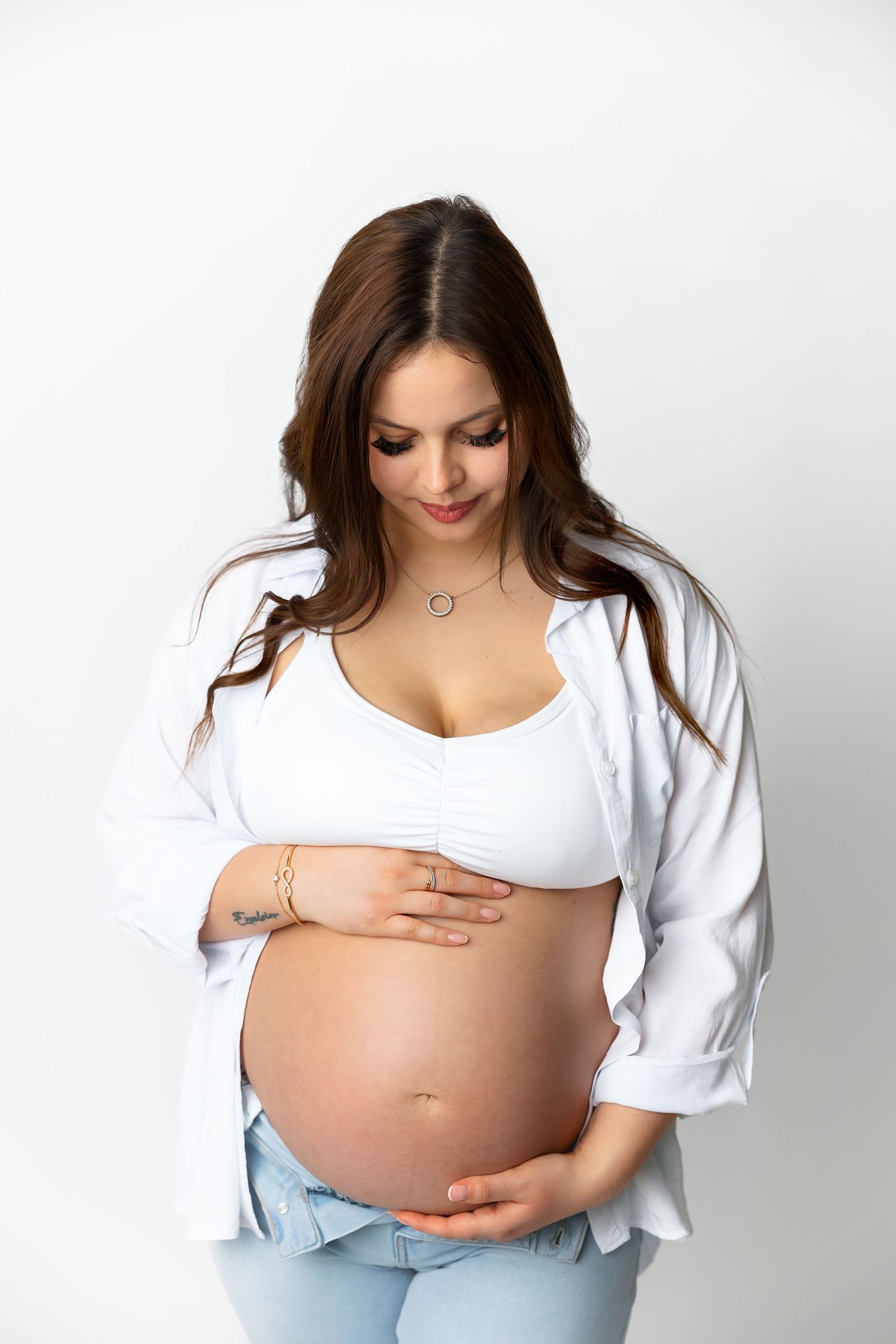 Expectant mother in white shirt showcases her baby bump against white background.