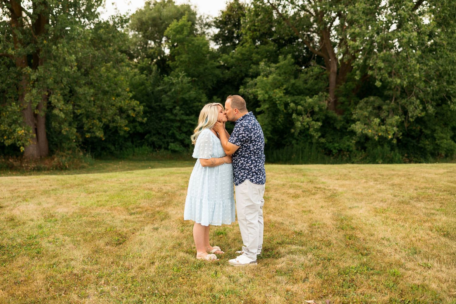 Couple embraces in a sweet moment on a lush grassy hill during a bright summer day.