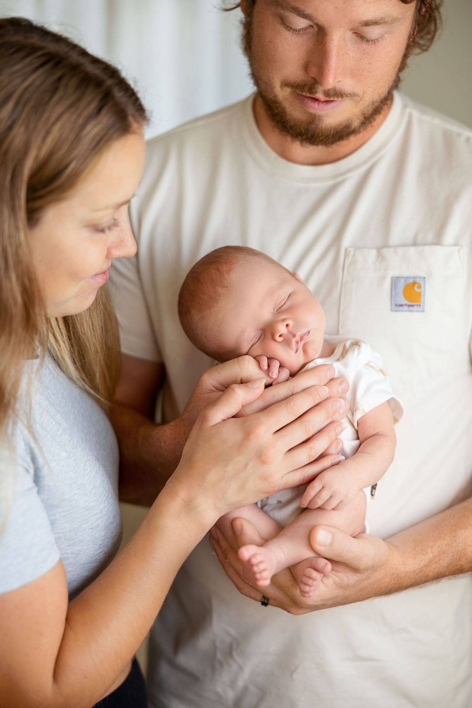 A couple in casual attire tenderly holds and kisses their newborn baby in a series of intimate lifestyle photos.