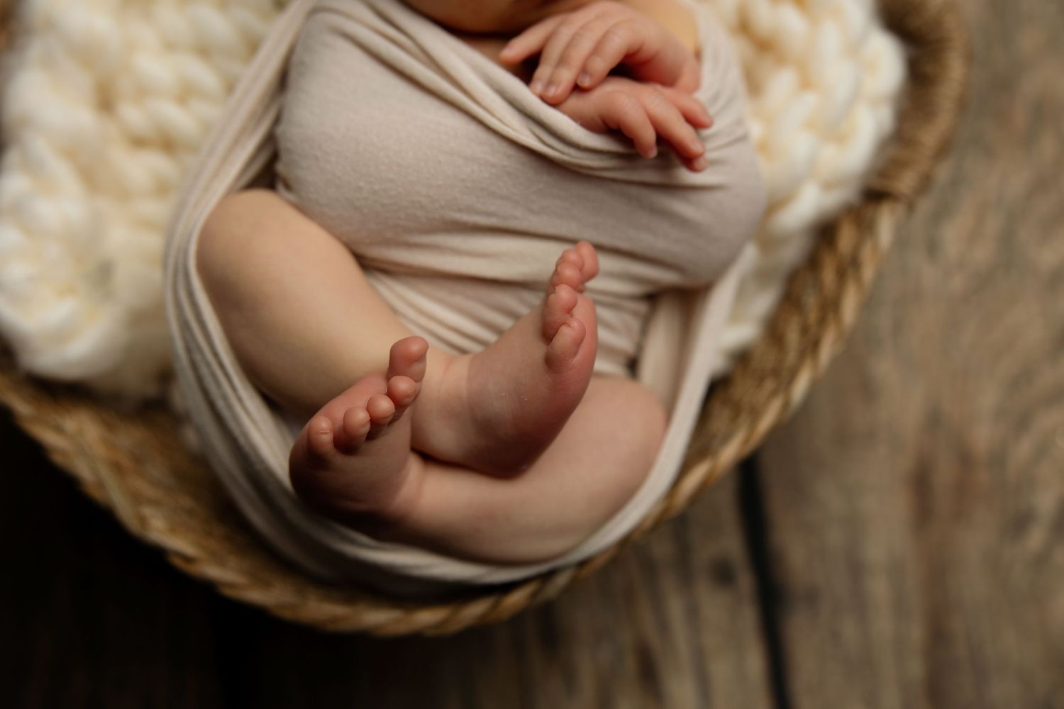 Closeup of newborn baby feet wrapped in beige fabric in wooden basket.
