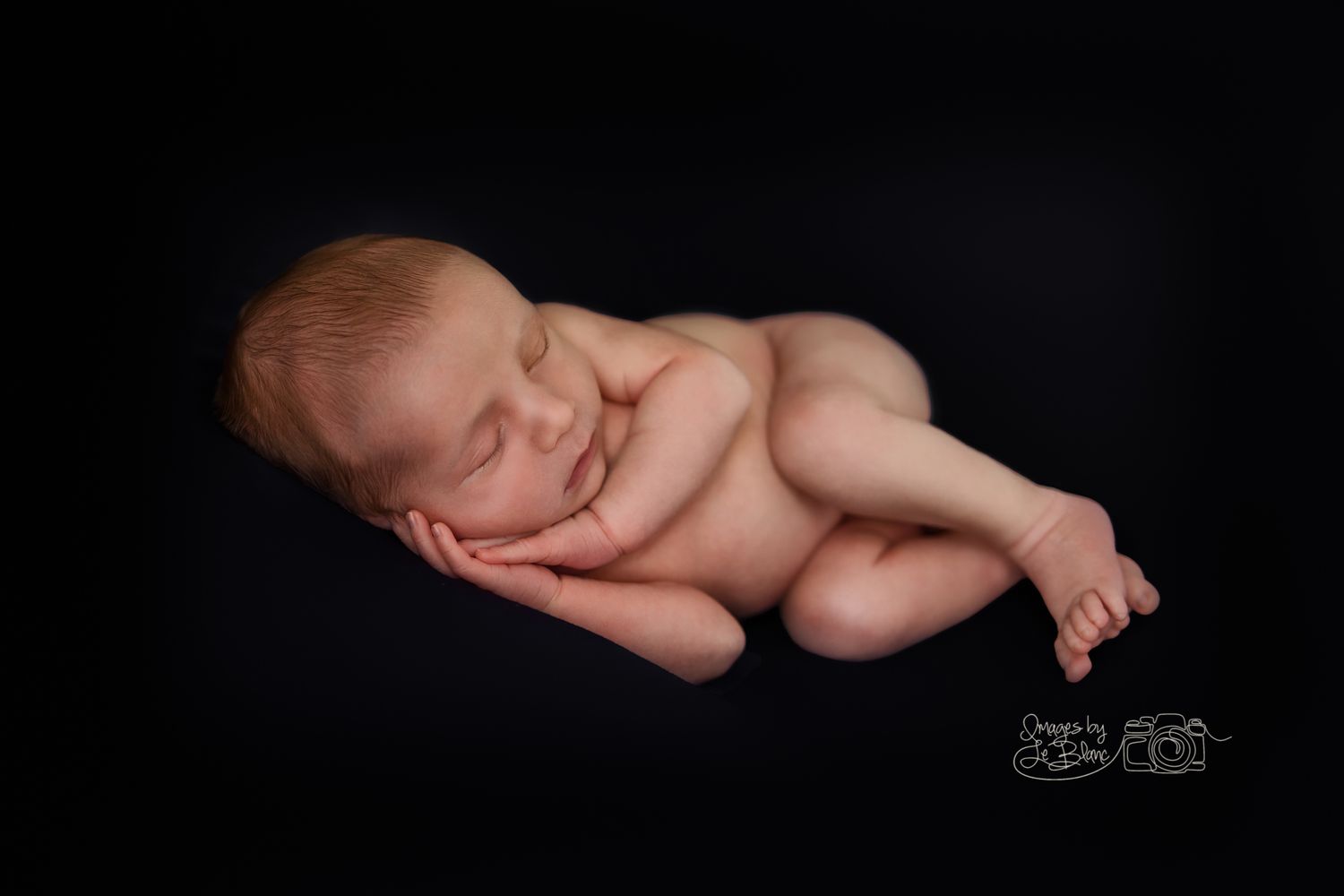 Peaceful sleeping newborn baby curled up on black background in artistic portrait.