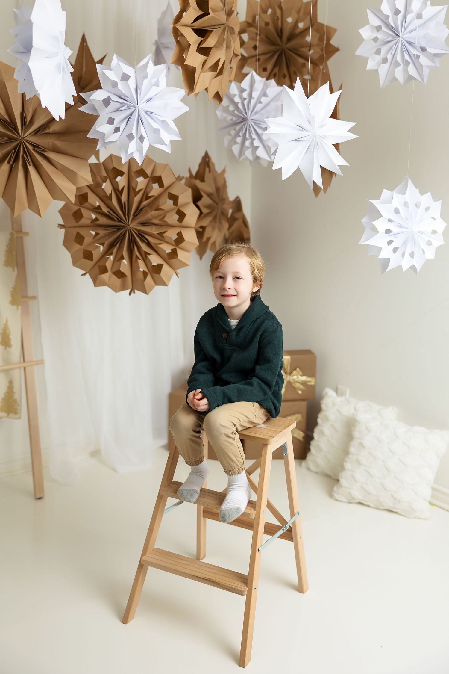 A winter-themed set with brown and white paper snowflakes hanging from above while a small figure sits on a wooden stool.