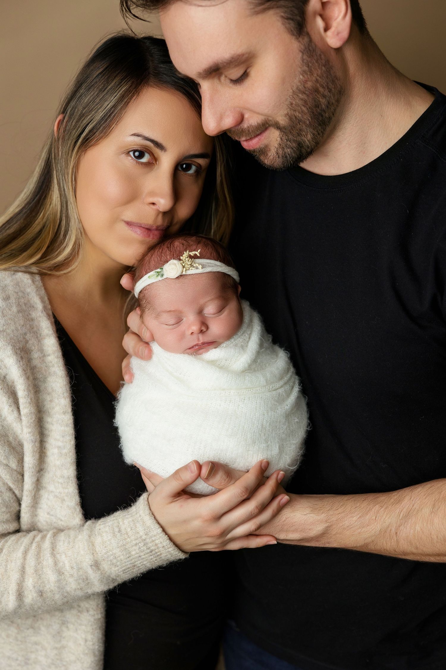 Parents lovingly embrace their swaddled newborn in studio portrait.
