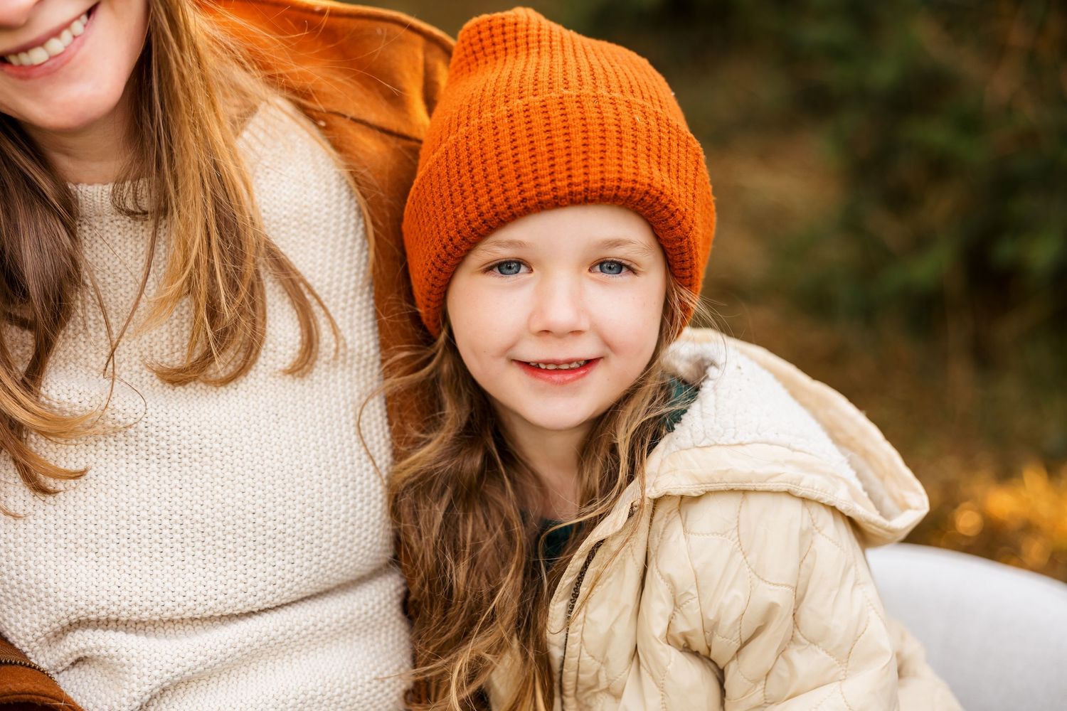 Child wearing orange knit beanie and cream colored jacket at Christmas tree farm.