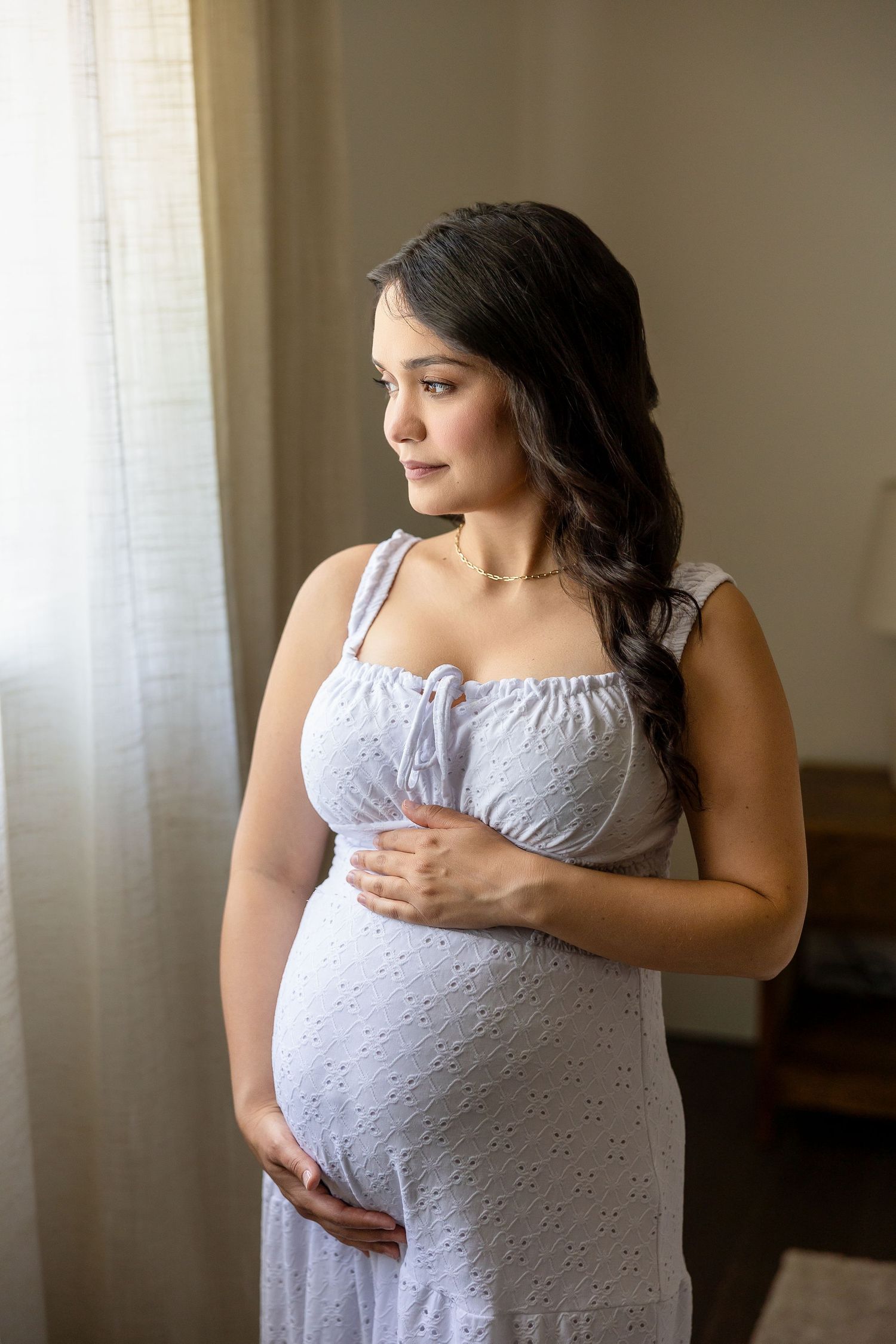A series of soft silhouetted maternity photos showing a woman in a white dress near a window.
