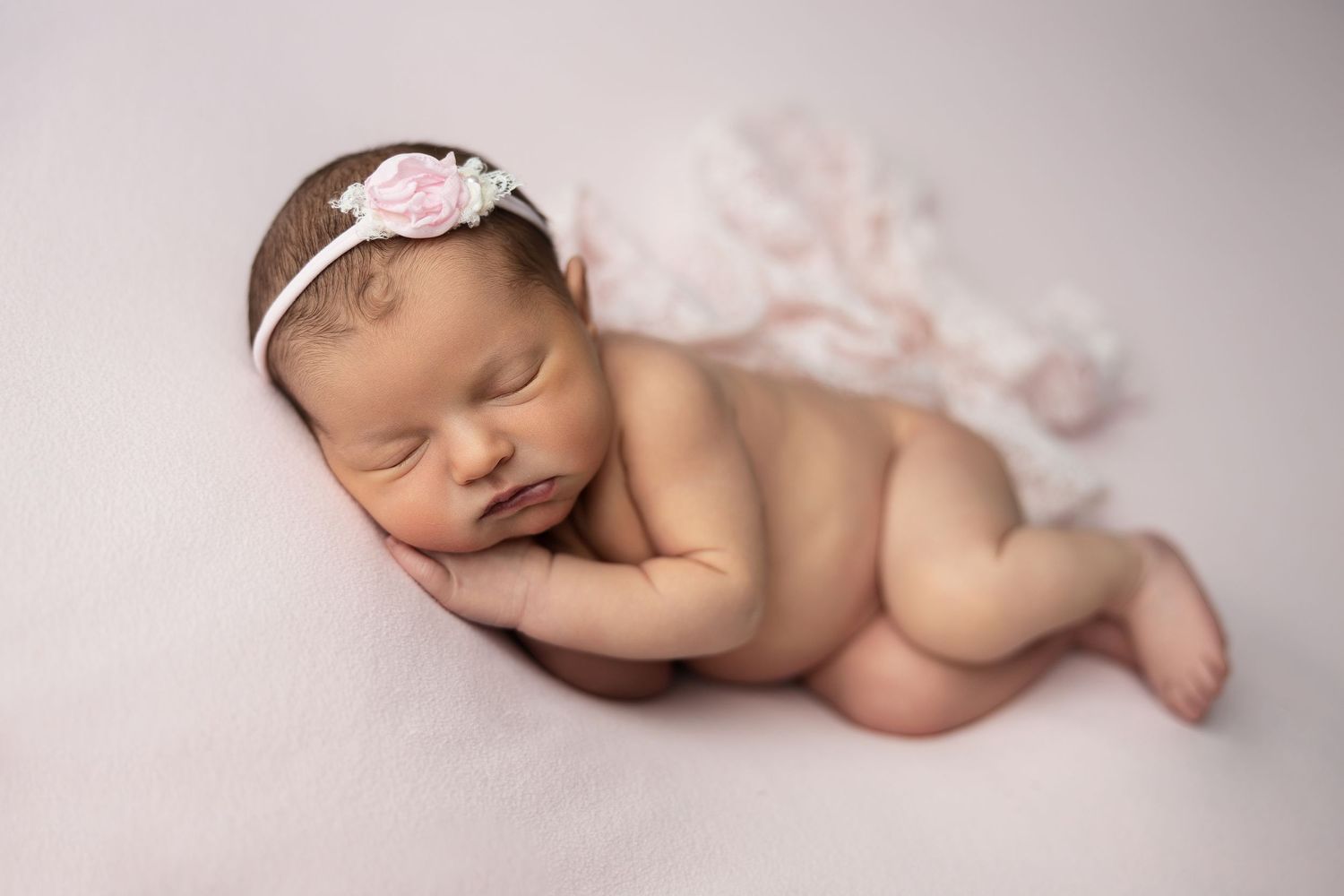 Peaceful sleeping newborn baby lying on soft pink blanket in professional studio portrait setting.