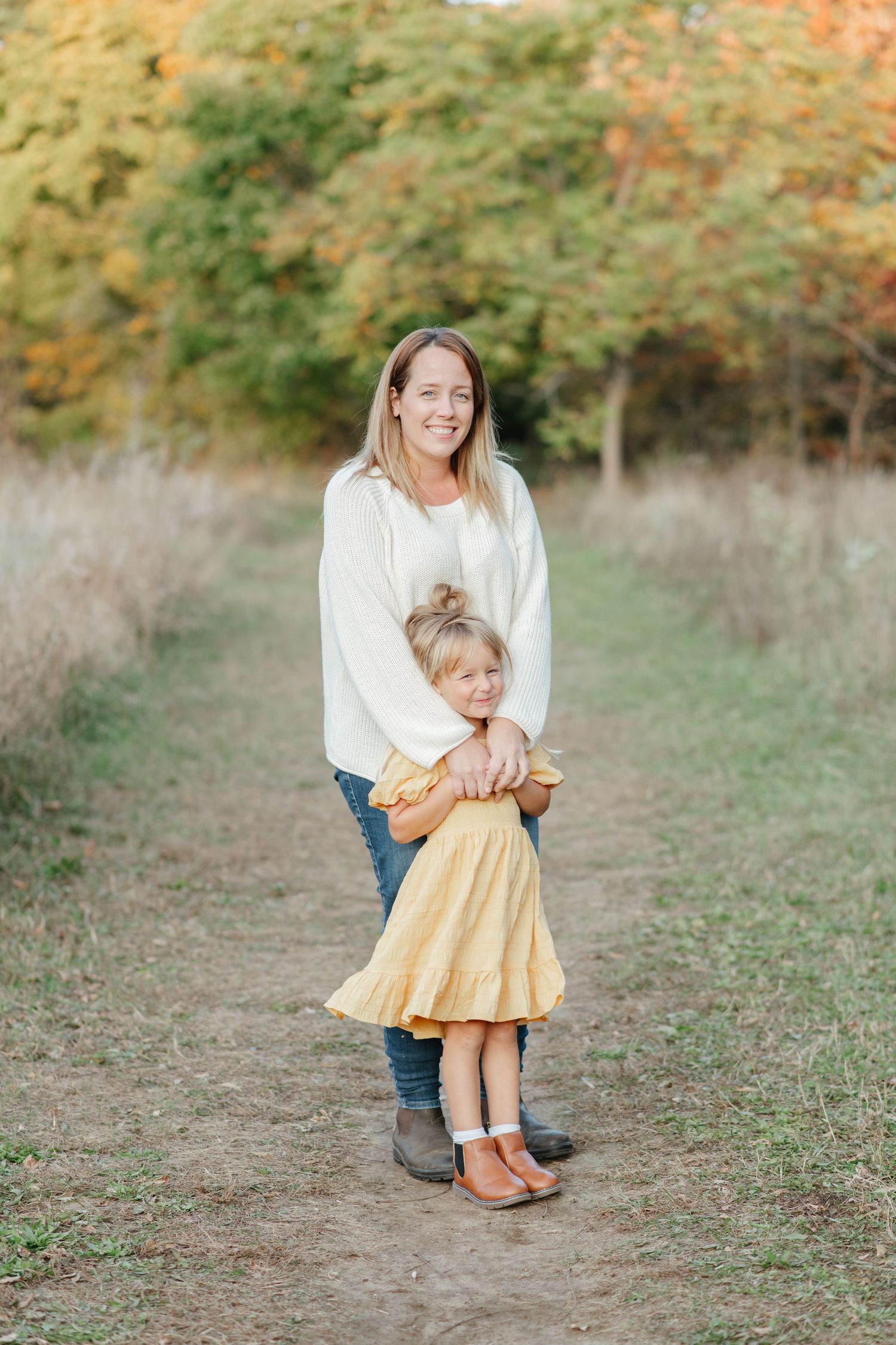 Two people share a tender moment together on a path surrounded by autumn foliage.