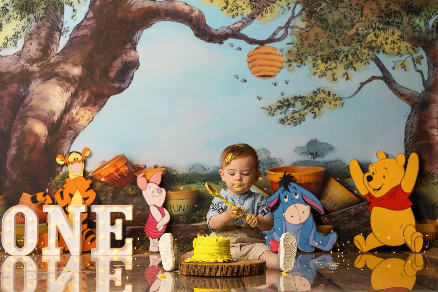 Winnie the Pooh themed first birthday setup with woodland backdrop and illuminated ONE sign.