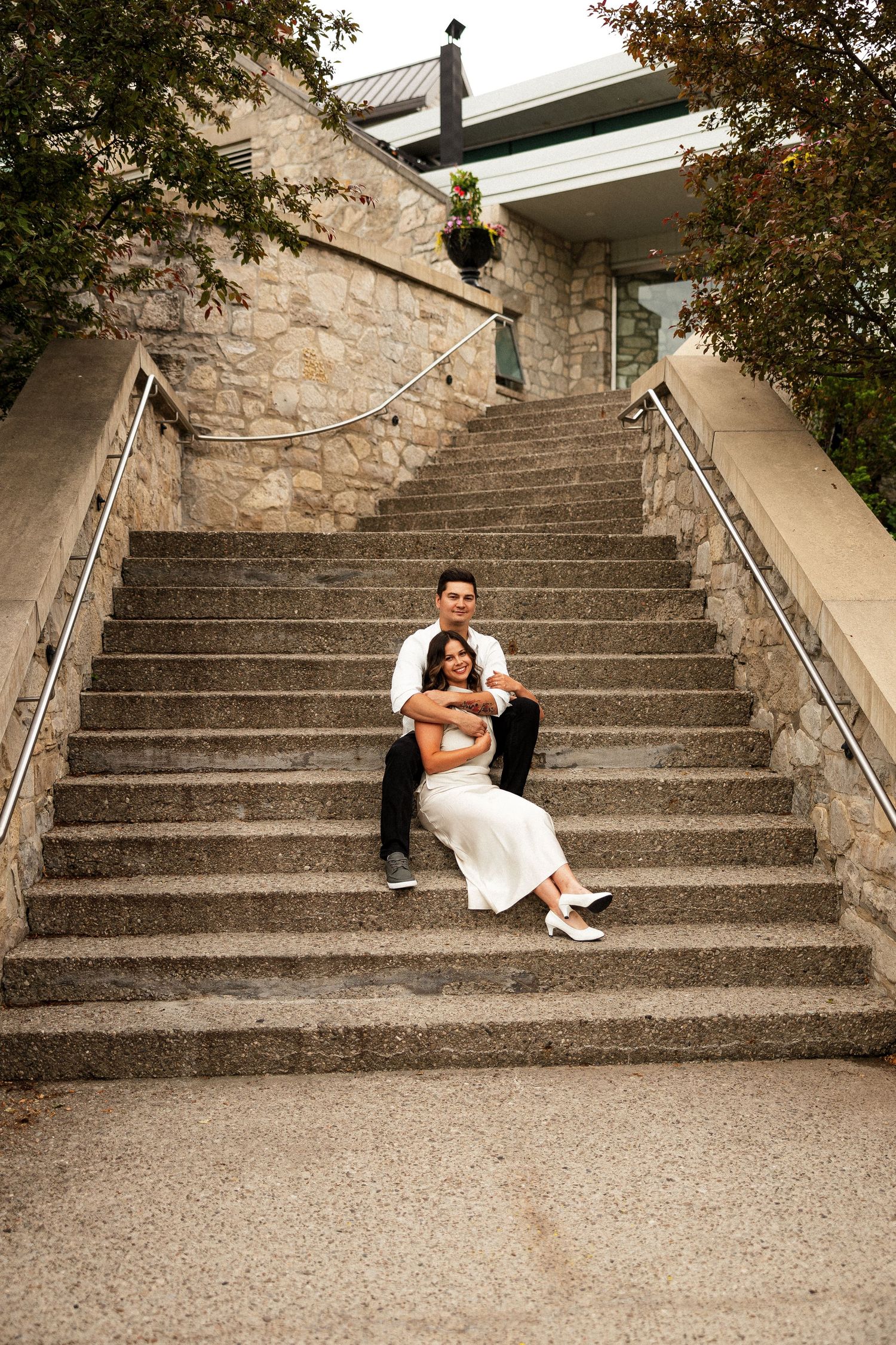 Bride and groom sitting together on stone steps, embracing in wedding attire outdoors.
