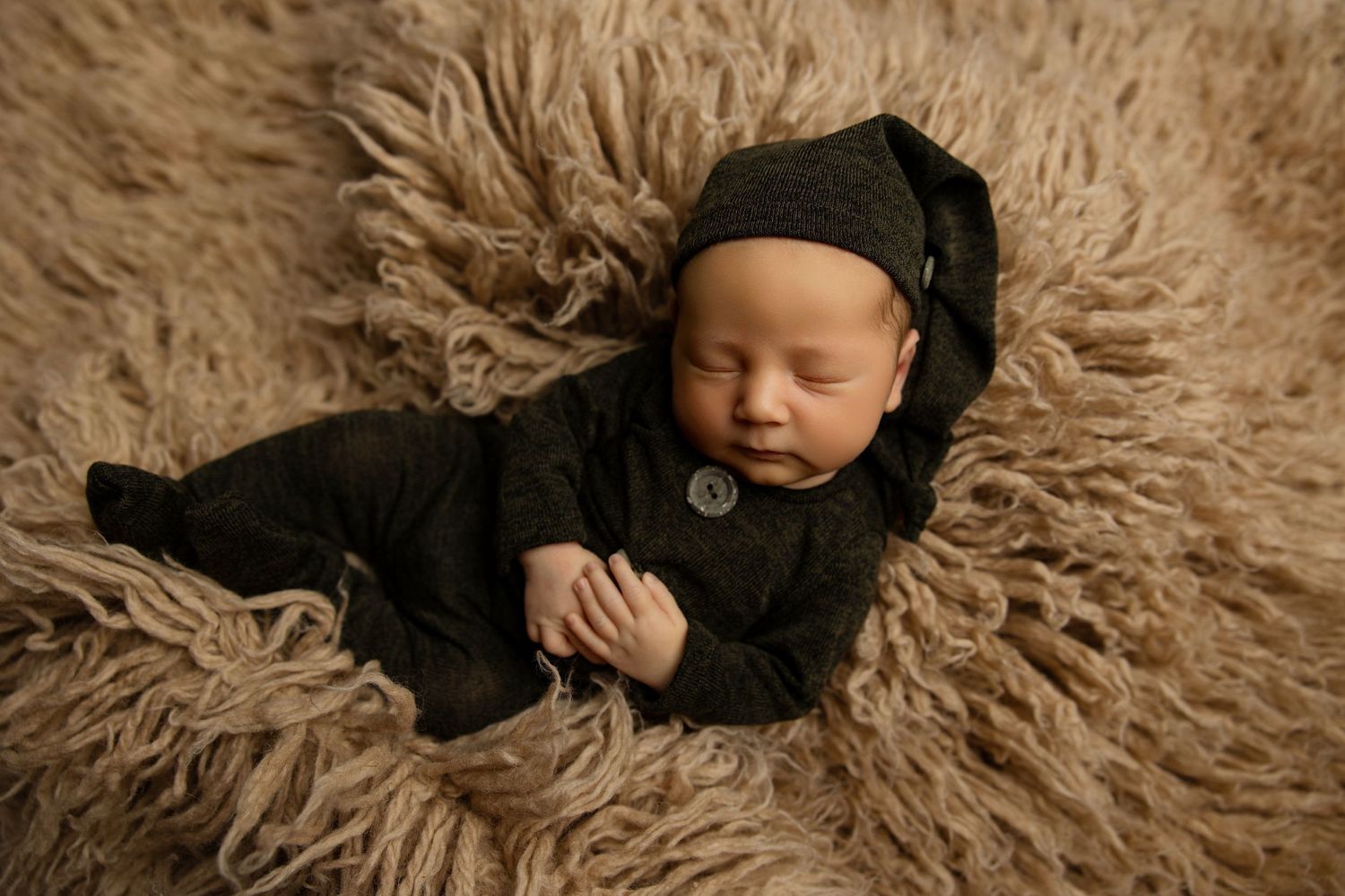 Sleeping newborn in black outfit lying on fluffy brown fur backdrop.