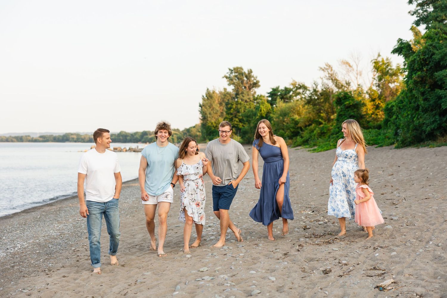 People strolling together on a sandy beach at golden hour with water and trees in background.