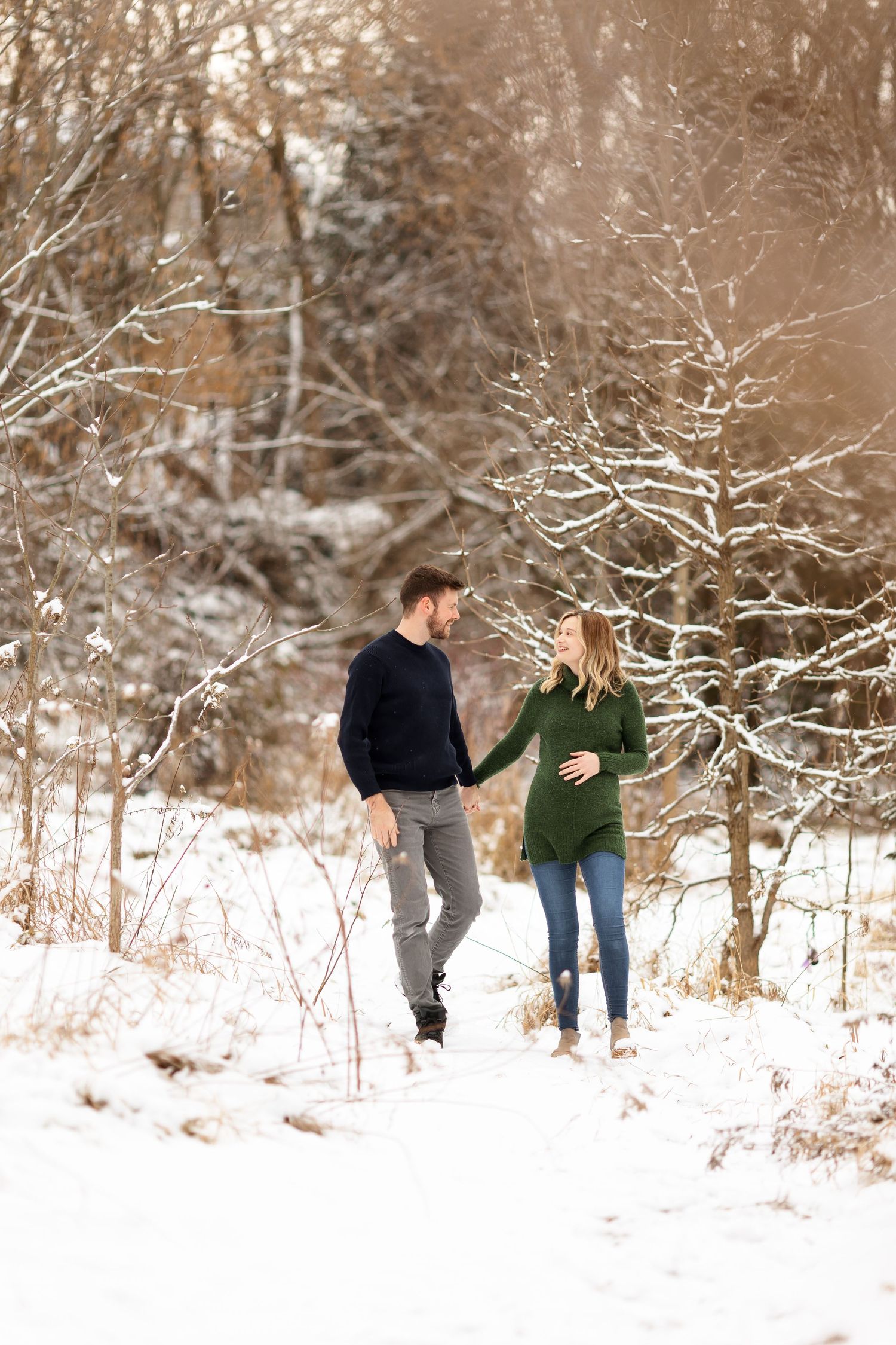 A couple walks hand in hand through a snow-covered forest path.