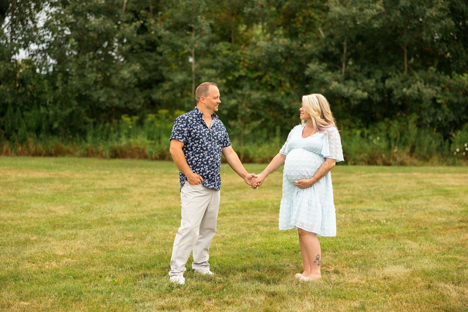A couple in blue and white outfits walk and hold hands romantically through a scenic outdoor field.